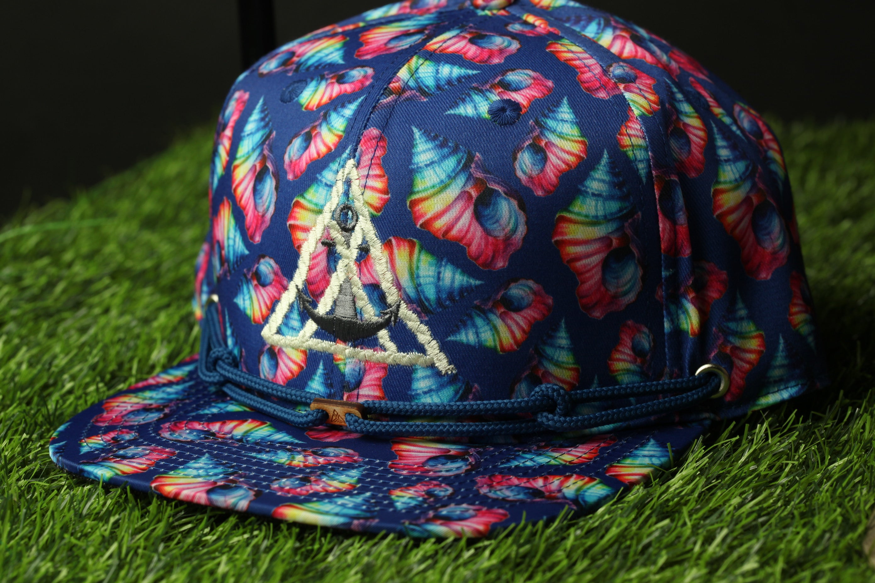 A colorful, patterned baseball cap with a floral design and a triangular emblem on the front, resting on a grassy surface.