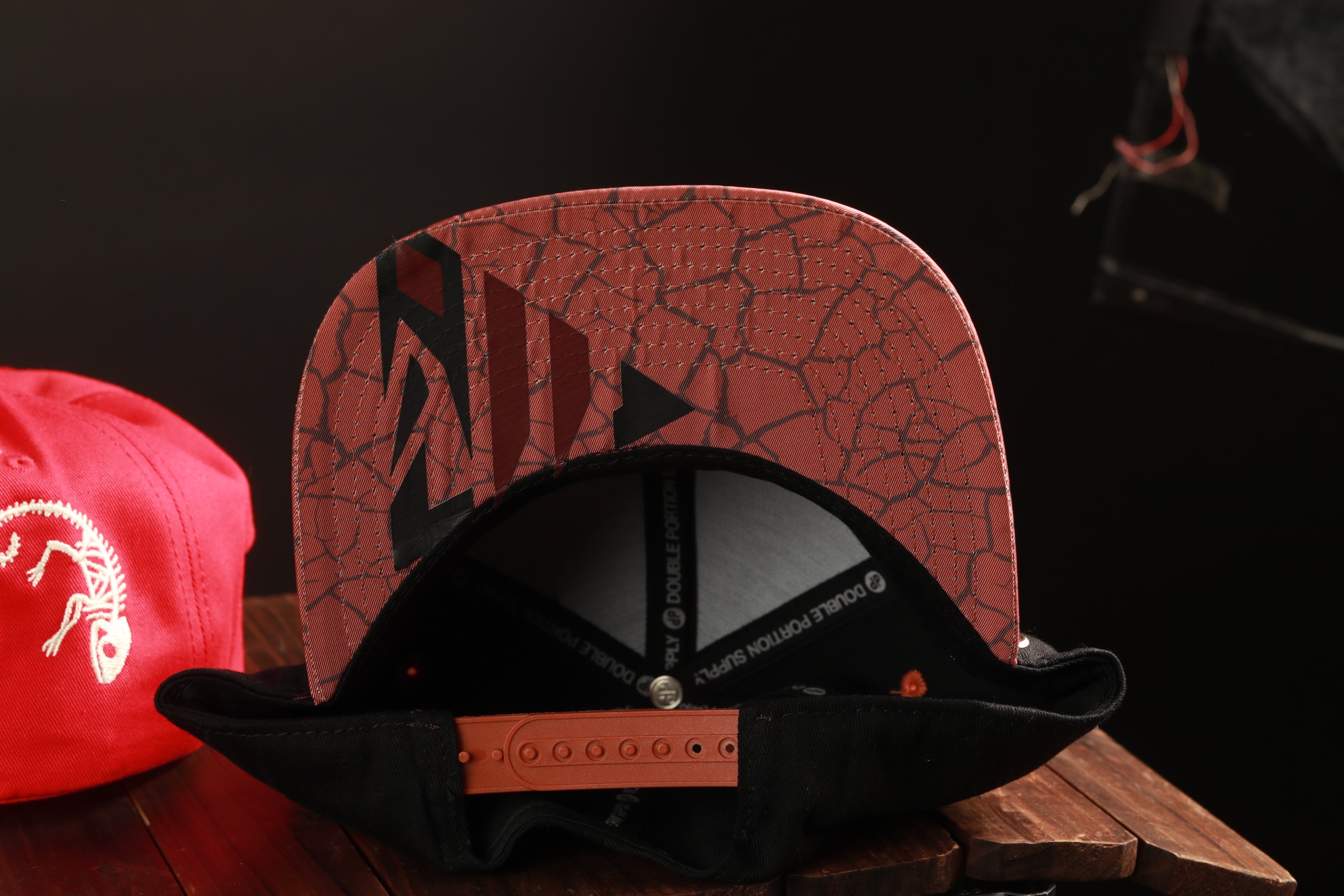 a red and black baseball cap with a cracked pattern, placed on a wooden surface next to a red baseball cap.