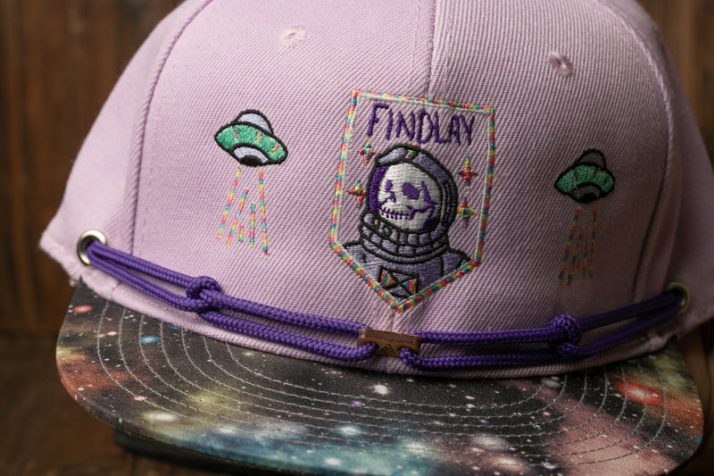A purple baseball cap with a space-themed design, featuring a skull and an alien spacecraft.