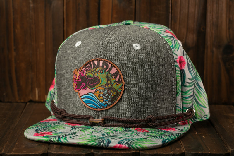 A gray baseball cap with a floral pattern and a circular patch on the front, placed on a wooden surface.