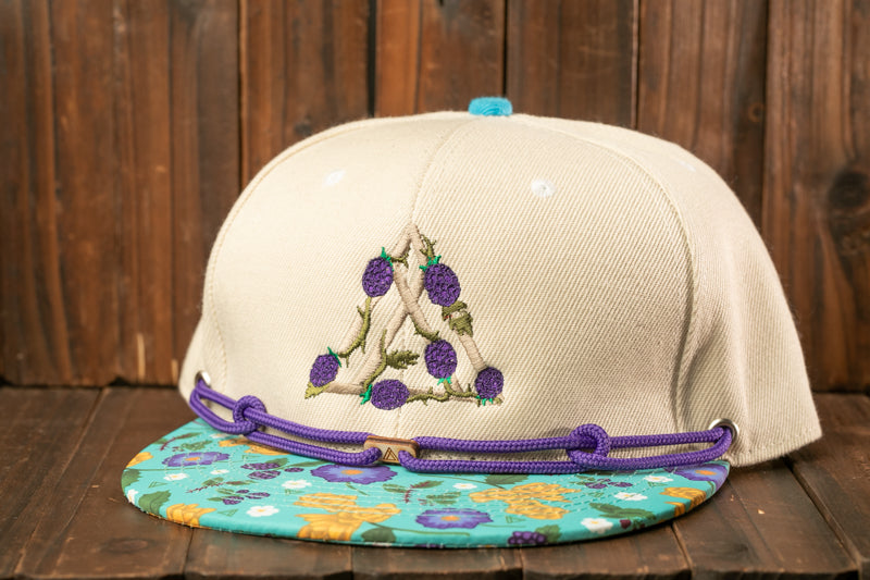 A beige baseball cap with a floral pattern and a blue brim, placed on a wooden surface.