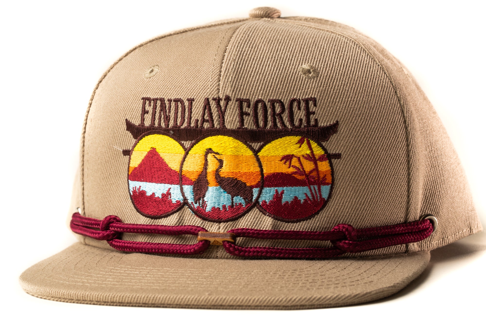 A tan baseball cap with a maroon adjustable strap and a graphic design featuring a bird silhouette and a sunset landscape.