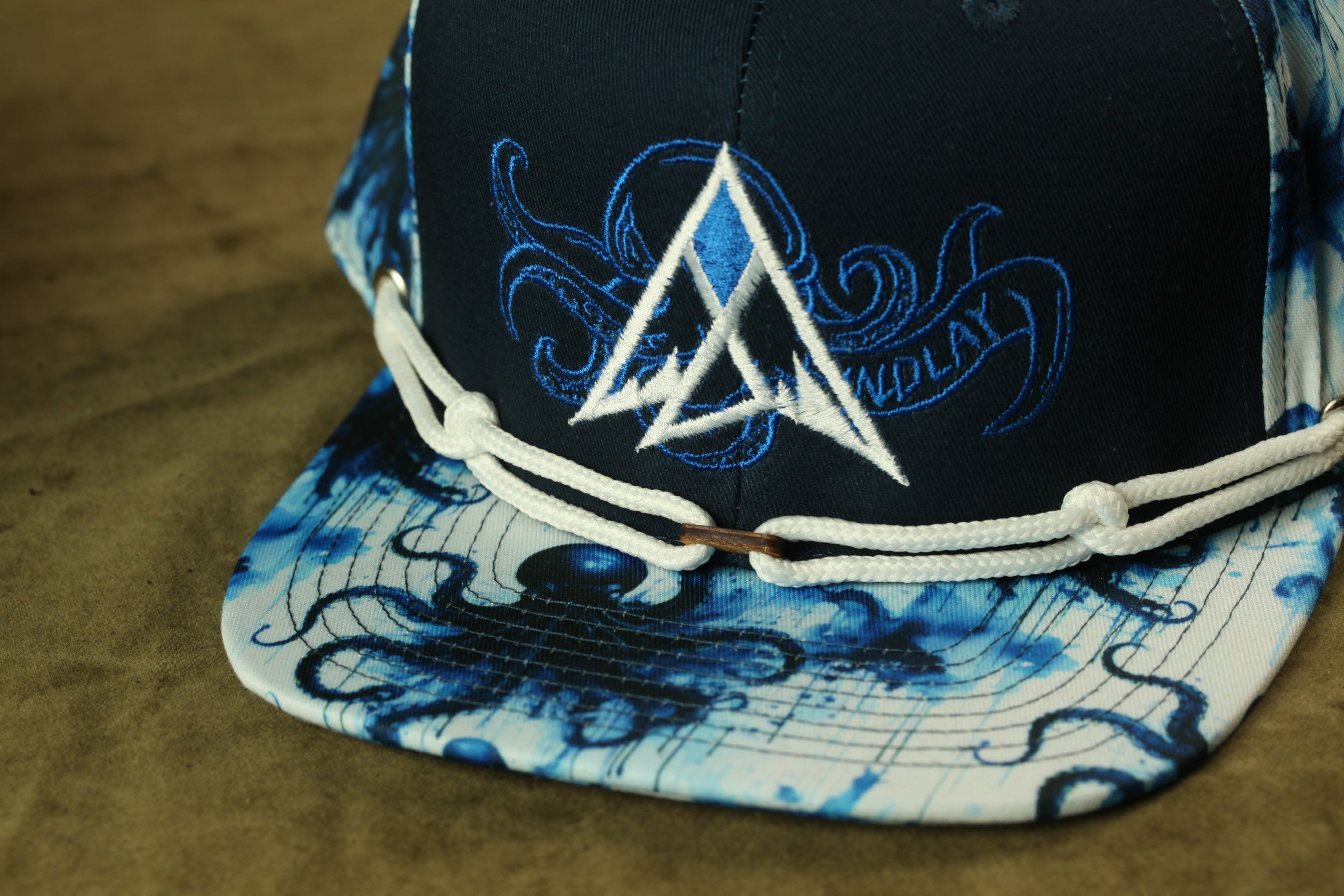 A close-up view of a black baseball cap with a blue and white patterned design, featuring a white triangle and an octopus motif.
