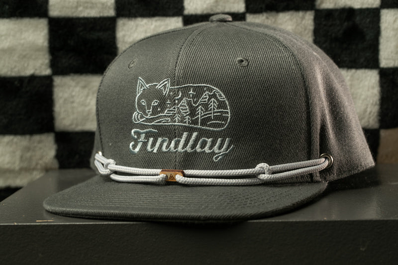 A gray baseball cap with a white embroidered design of a cat and the word "Findlay" on it, along with a white string or strap.