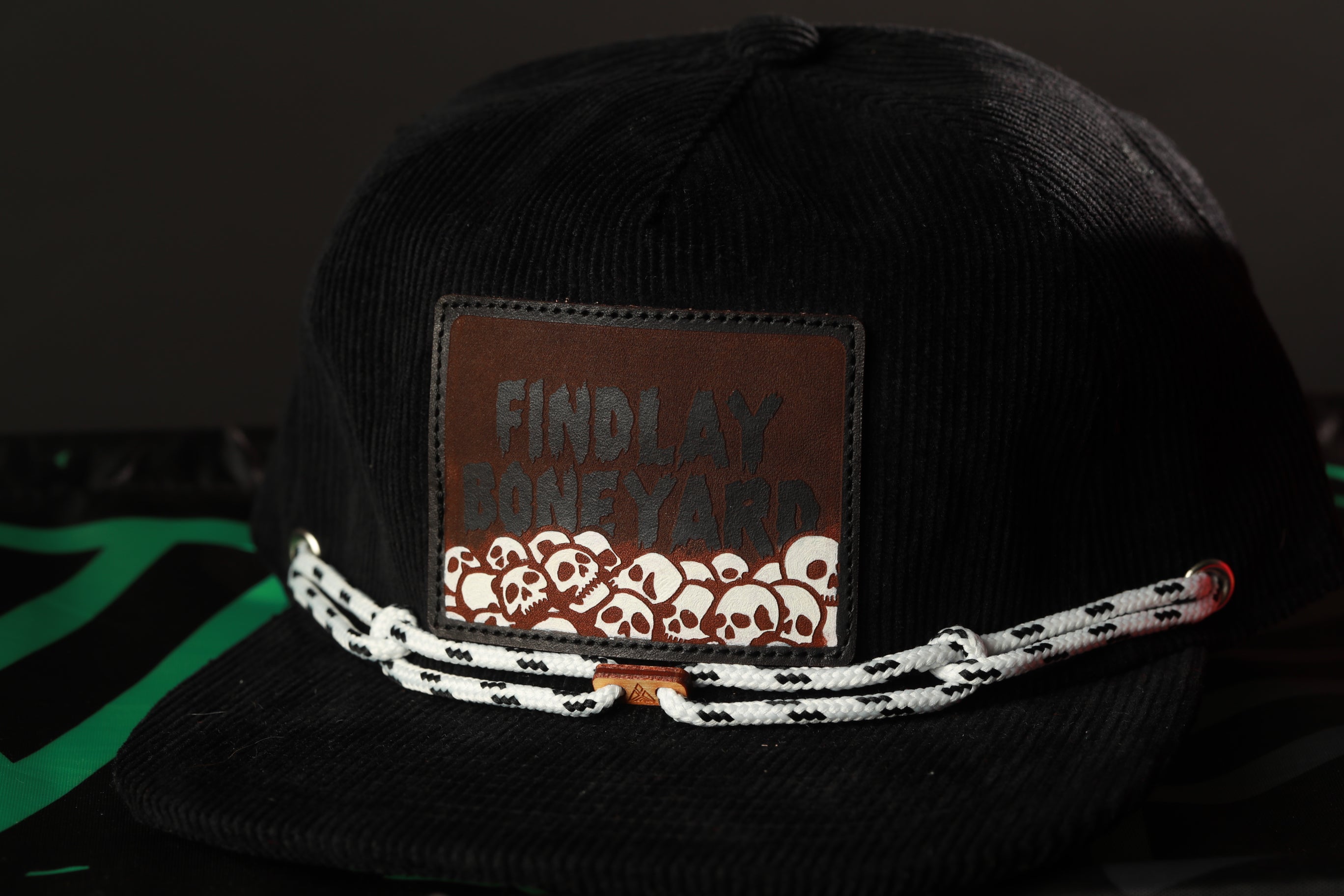 A black baseball cap with a brown patch on the front displaying the text "FIND LAY BONEYARD" and a white skull design.