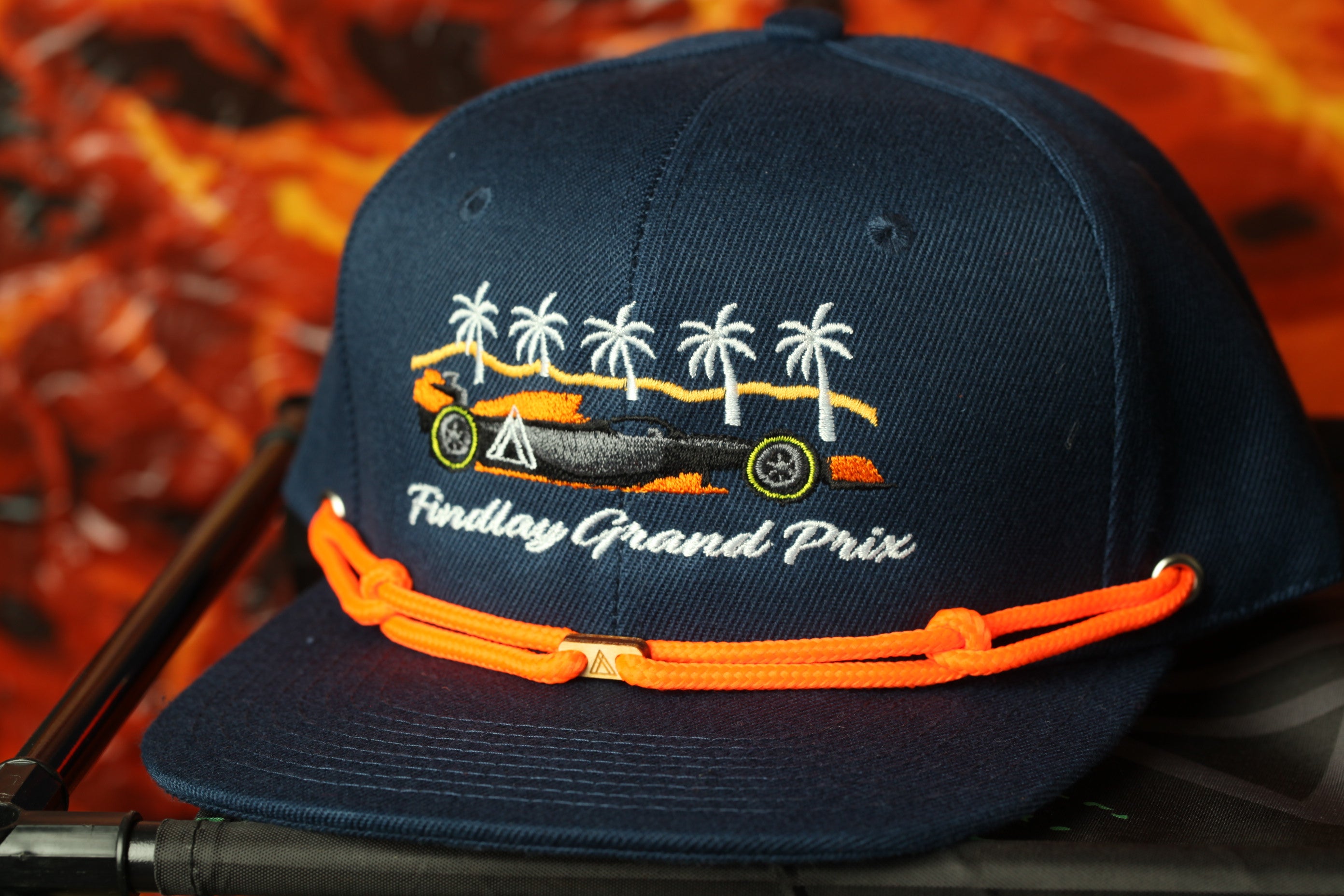 A navy blue baseball cap with an embroidered design of a race car and palm trees, along with the text "Findlay Grand Prix".