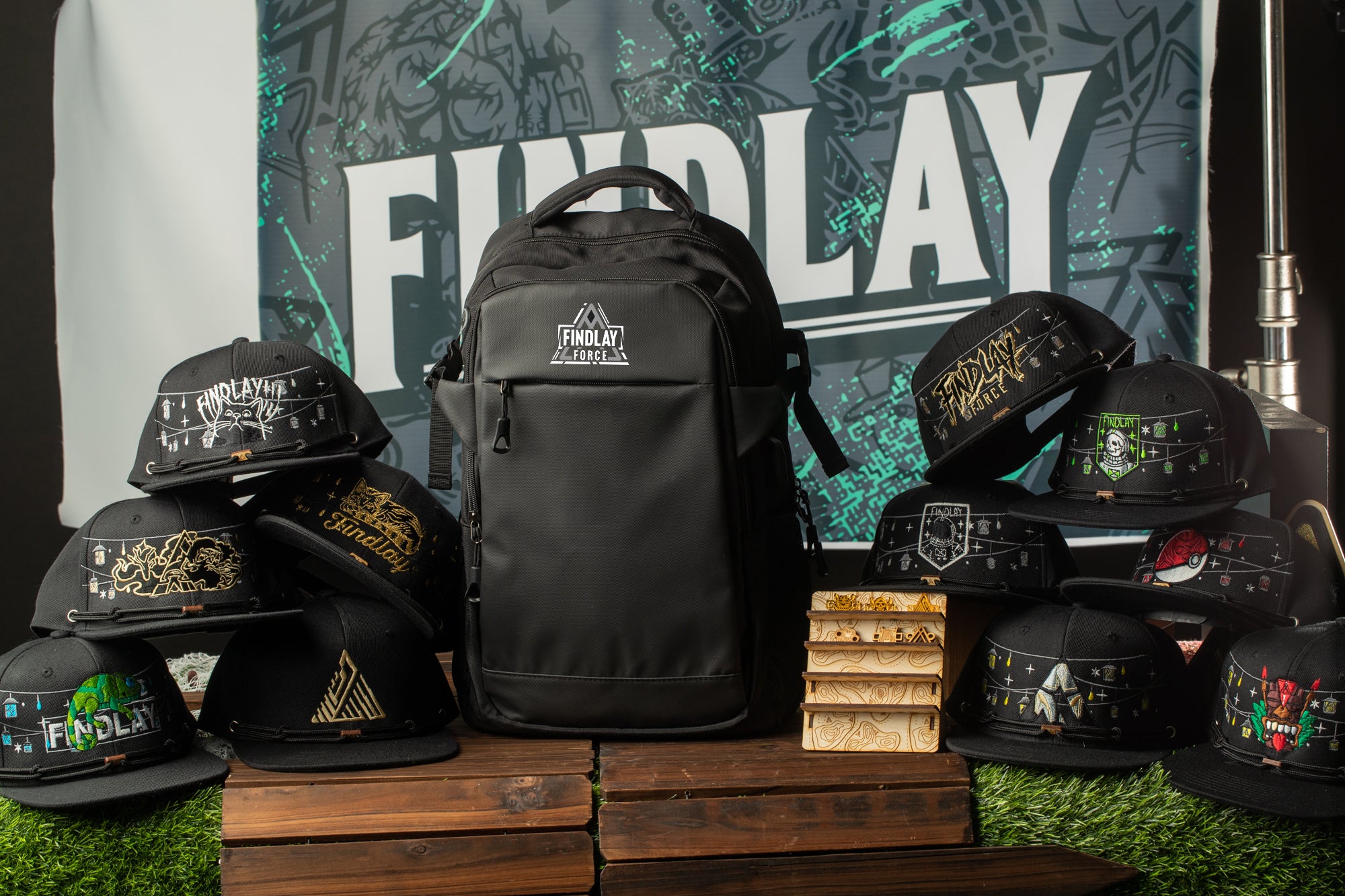A collection of black baseball caps and a backpack are displayed against a black and green background with the word "FINDlay" prominently featured.