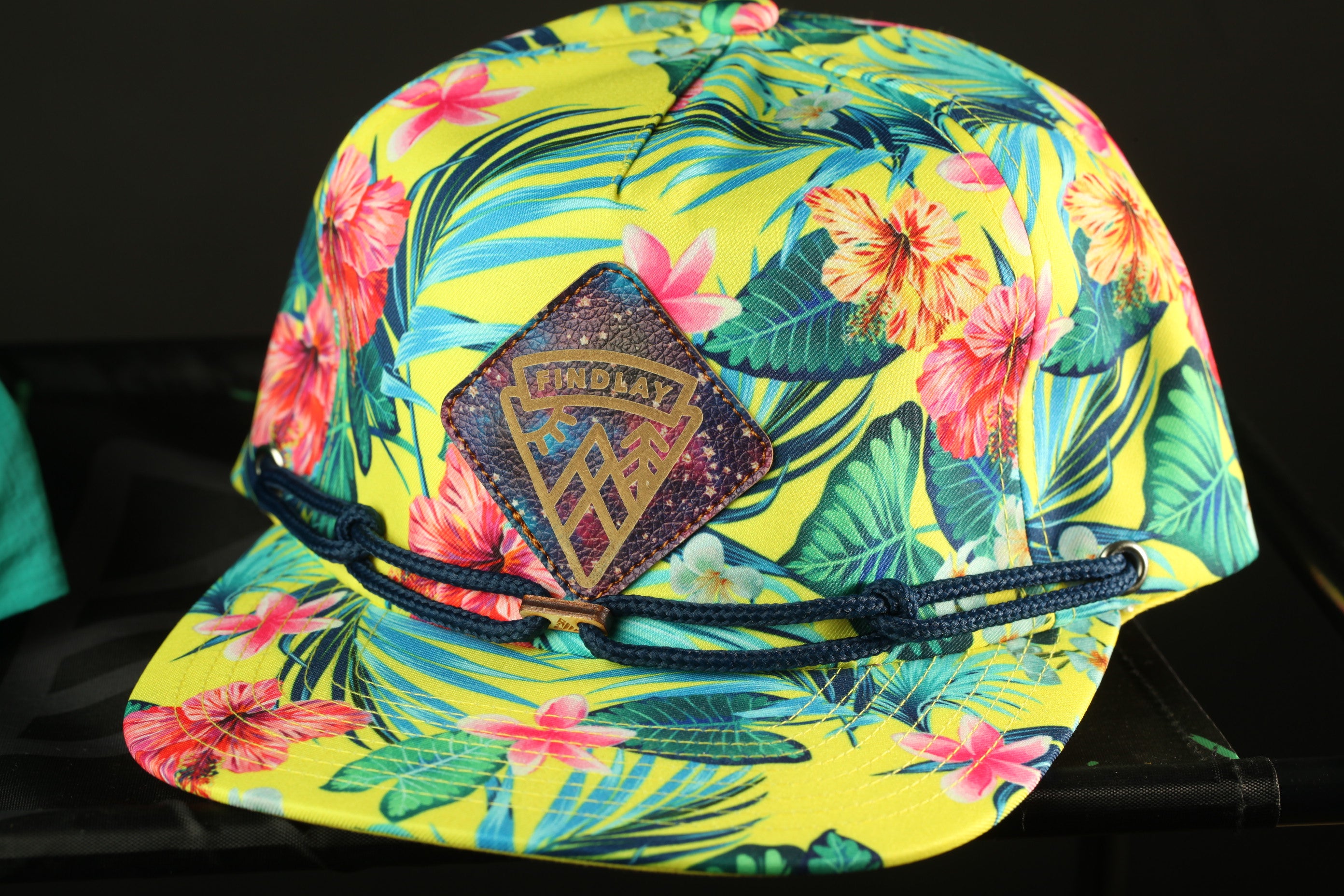 A colorful tropical-themed baseball cap with a floral pattern and a diamond-shaped patch on the front.