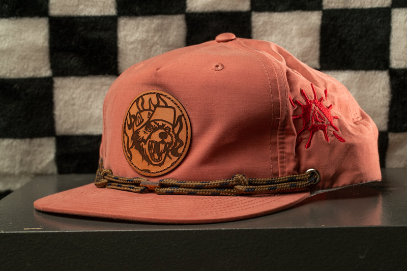 A pink baseball cap with a brown embroidered logo on the front, featuring a stylized dog or wolf design.