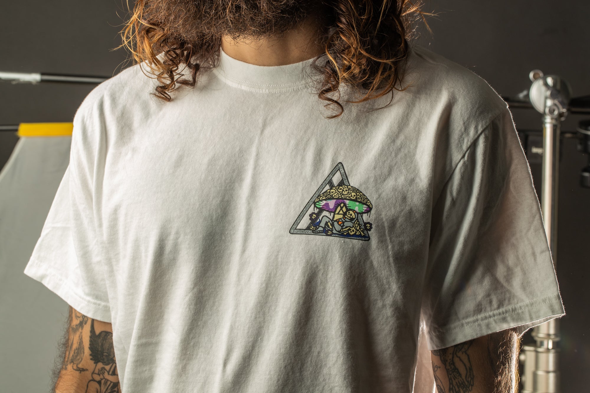 A person with long hair wearing a white t-shirt with a colorful graphic design on the front.