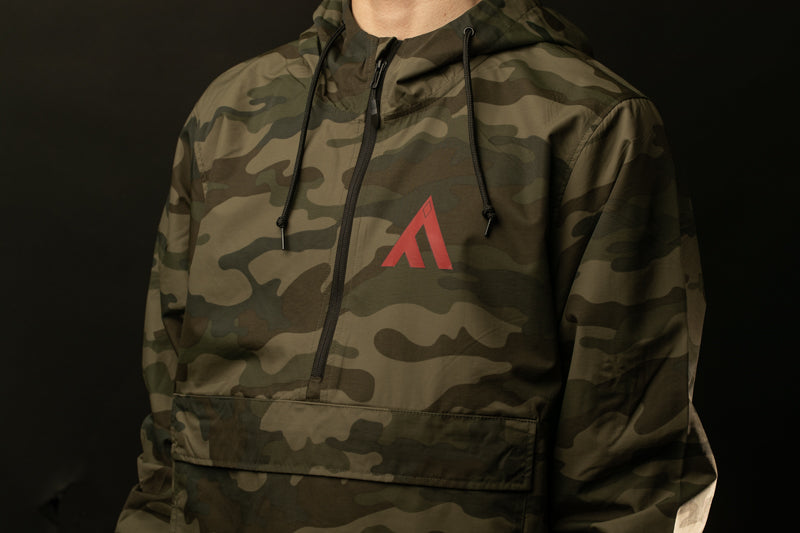 A person wearing a camouflage jacket with a red triangle logo on the chest.