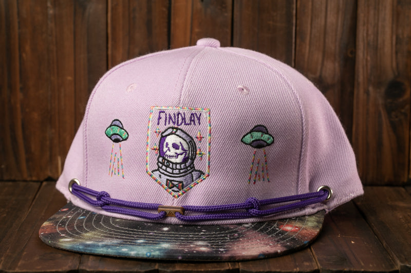 A purple baseball cap with a space-themed design, including a skull wearing a spacesuit and two alien spacecraft.