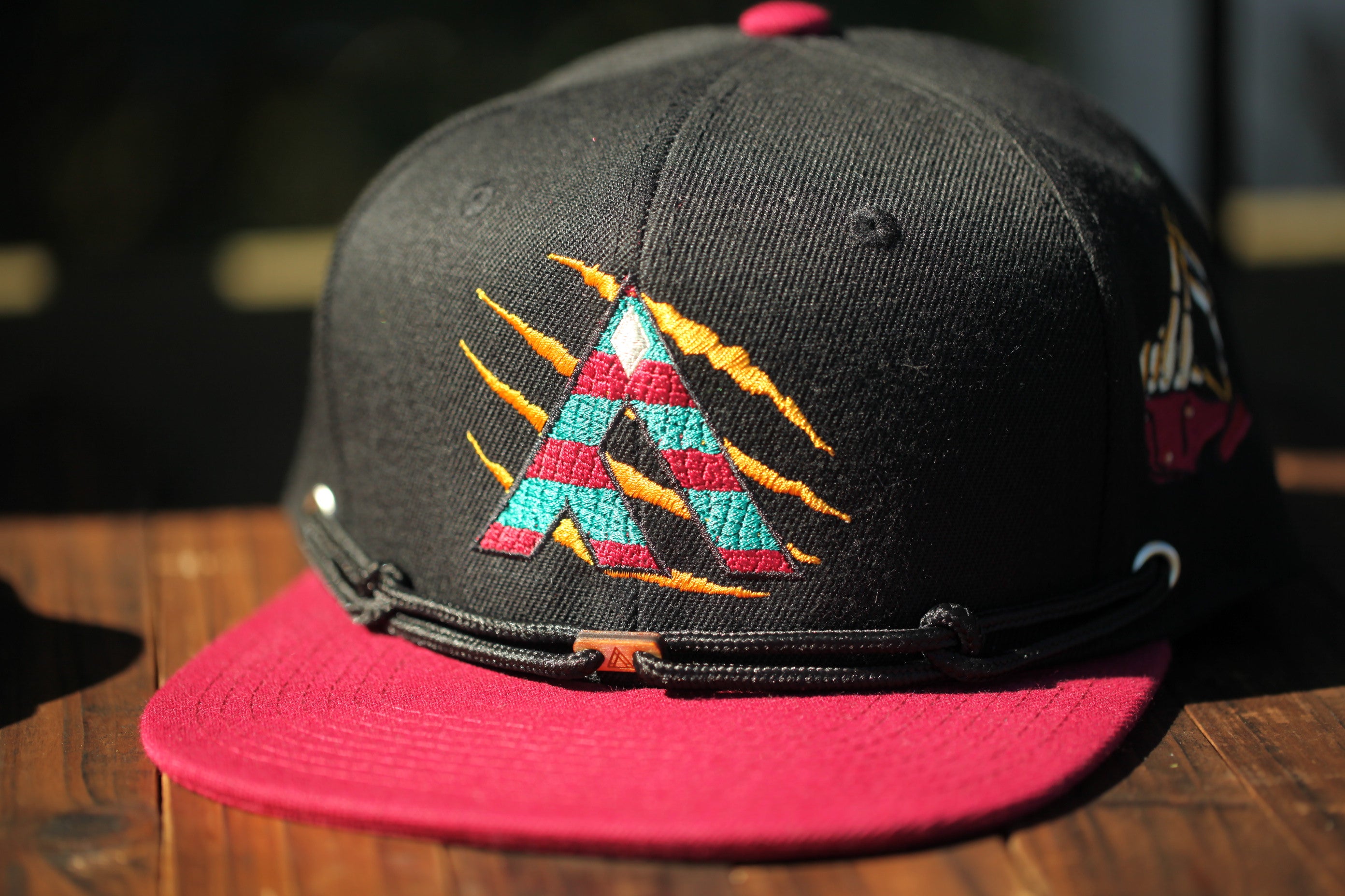 A black baseball cap with a red brim and a colorful embroidered logo on the front.