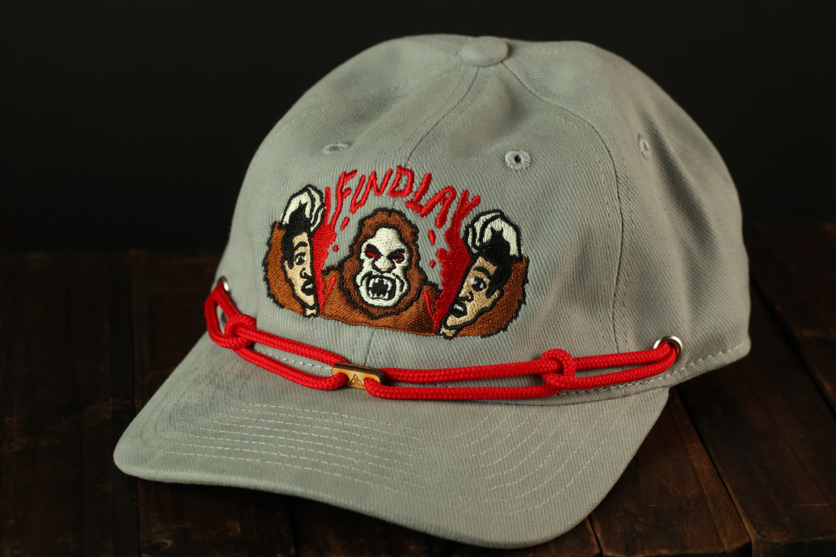 A gray baseball cap with a red string and an embroidered design featuring three cartoon-like faces.