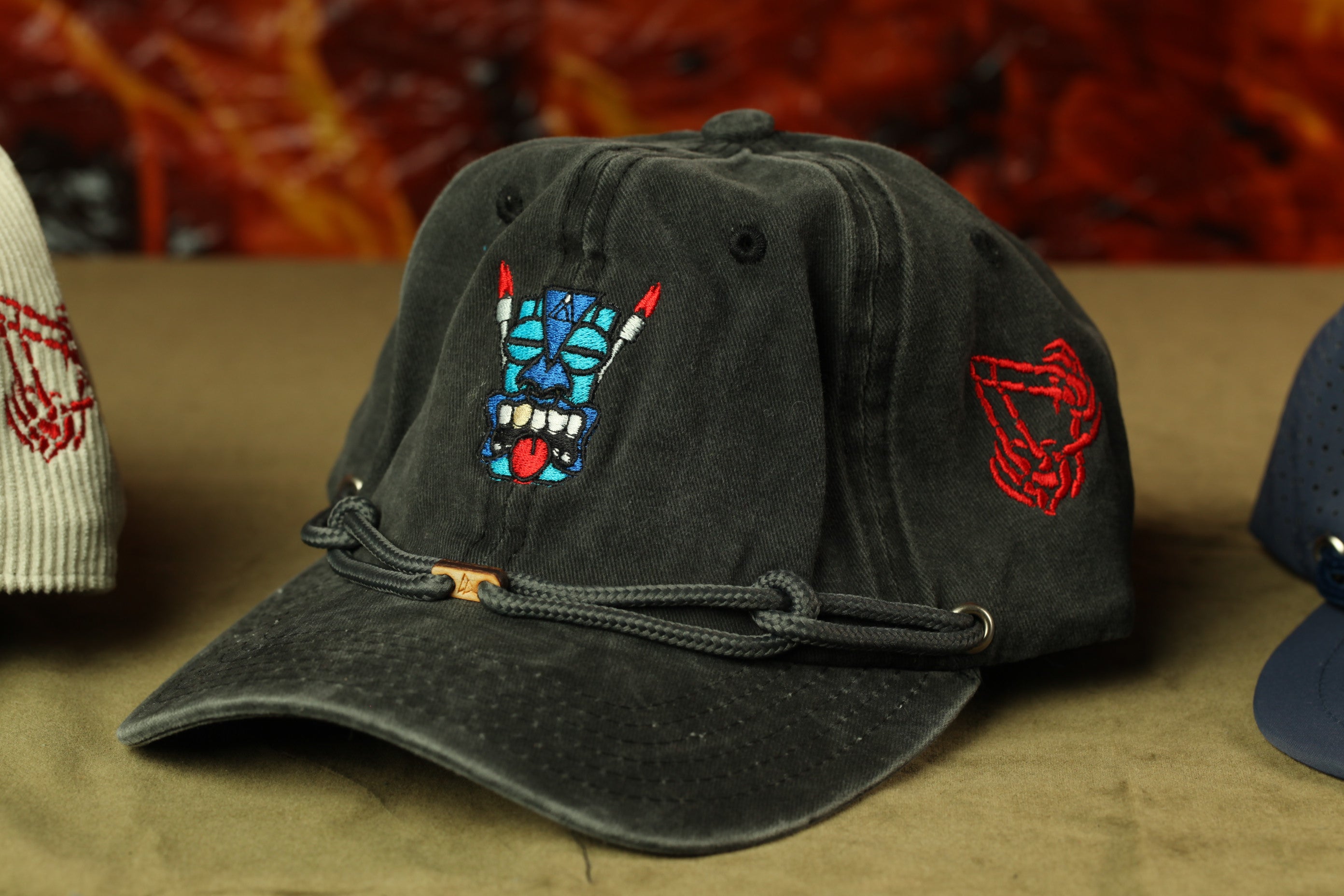 A black baseball cap with a colorful design on the front, including a skull and crossbones motif, is displayed on a table.