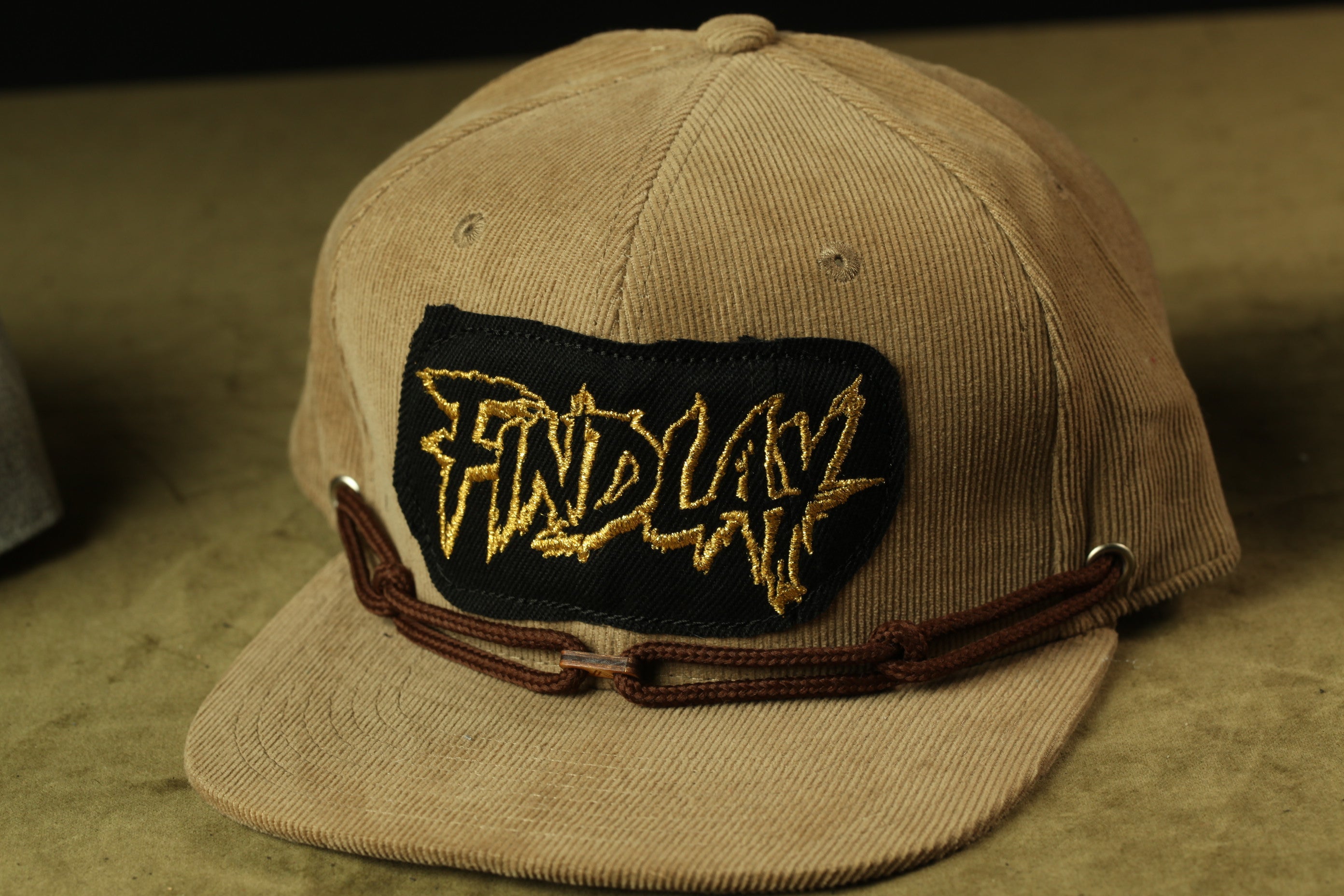 A beige baseball cap with a black patch on the front displaying the word "FIND" in a stylized font.