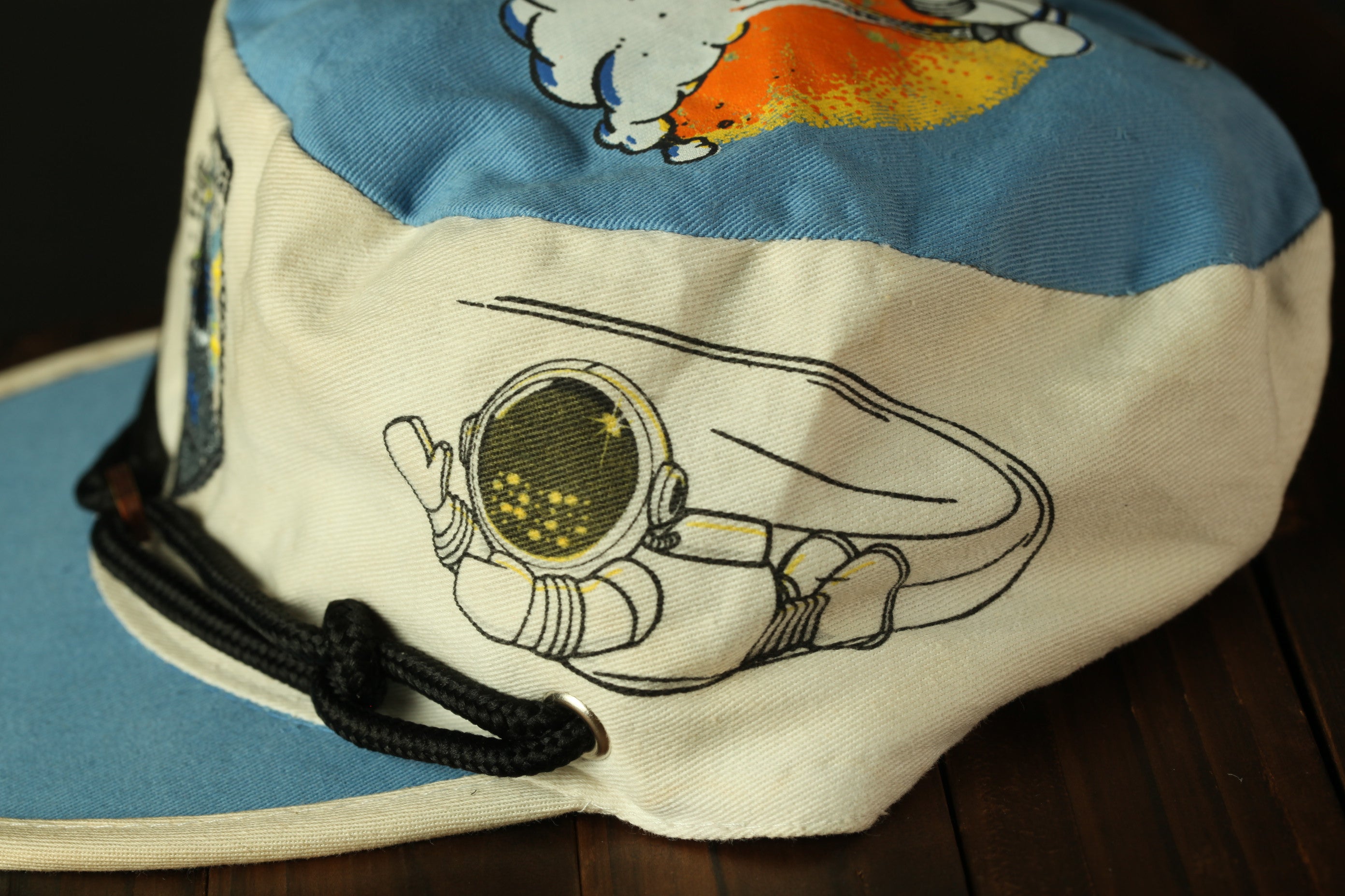 A close-up view of a cap with a cartoon astronaut design on it.