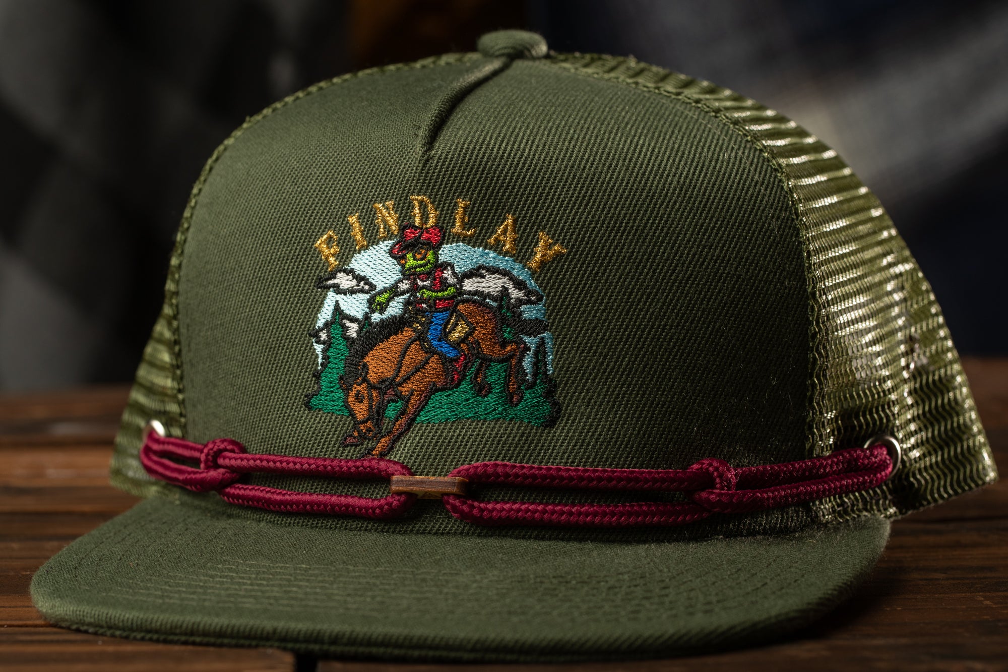 A green baseball cap with a graphic of a cowboy riding a bucking bronco on the front.