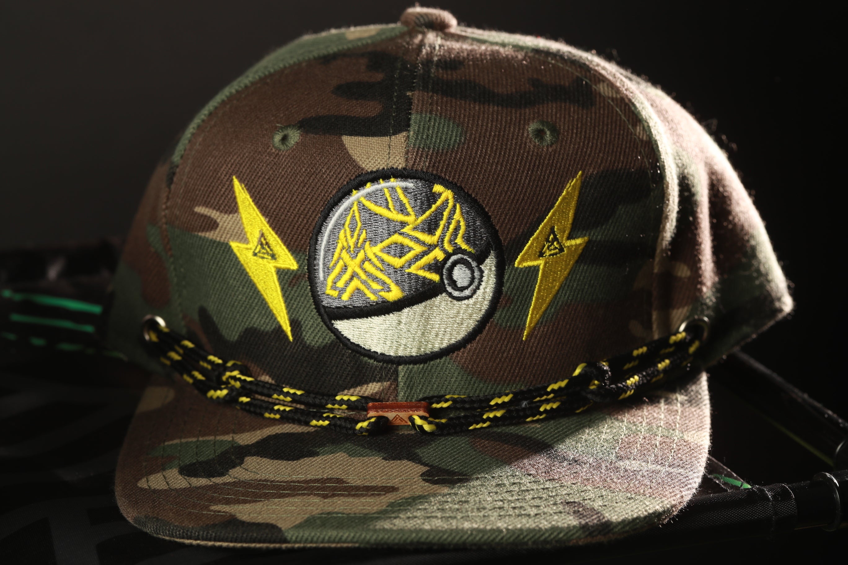 A camouflage baseball cap with a Pokemon-inspired design, including a lightning bolt symbol and a Pokemon ball.