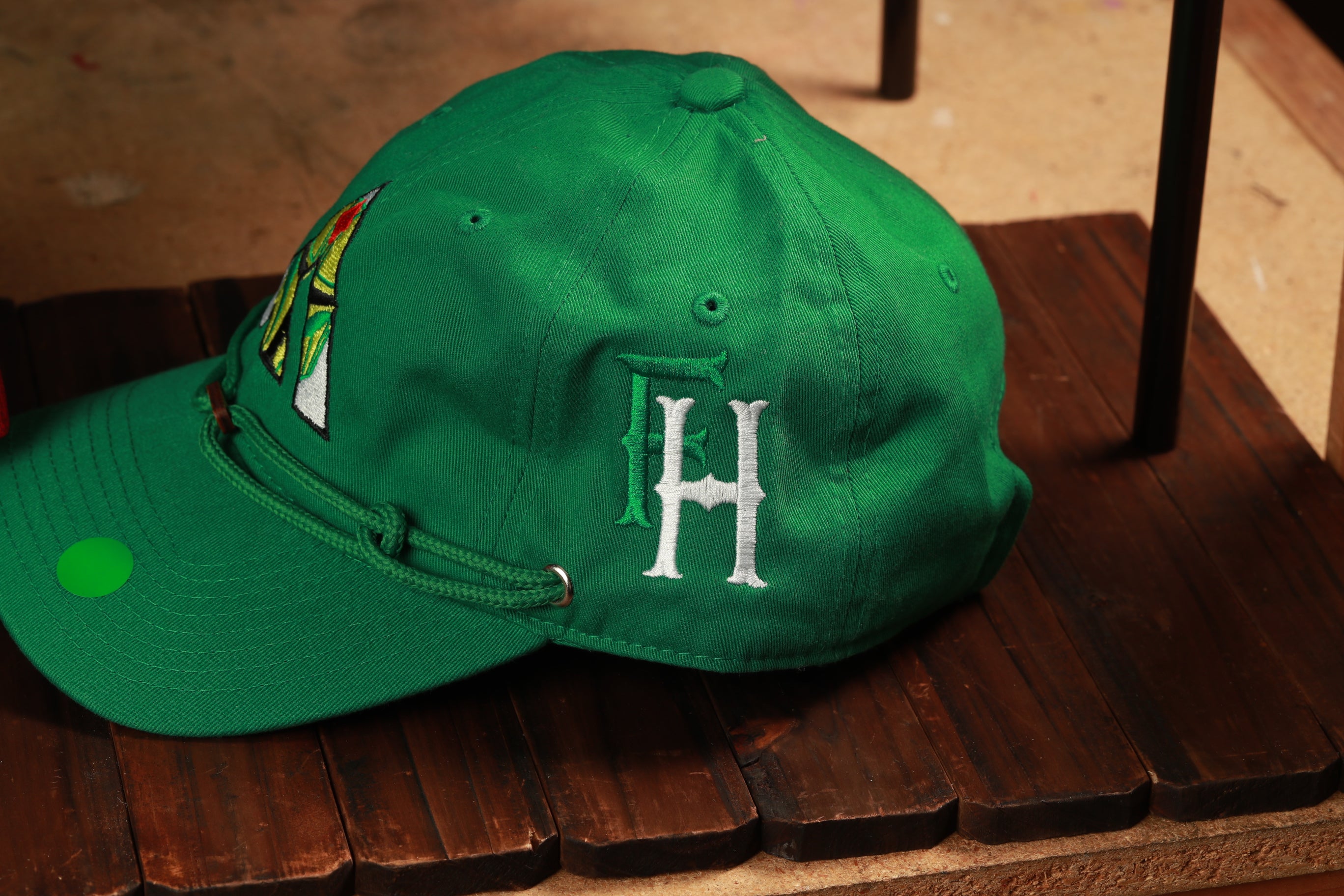 A green baseball cap with a white "H" embroidered on it, resting on a wooden surface.