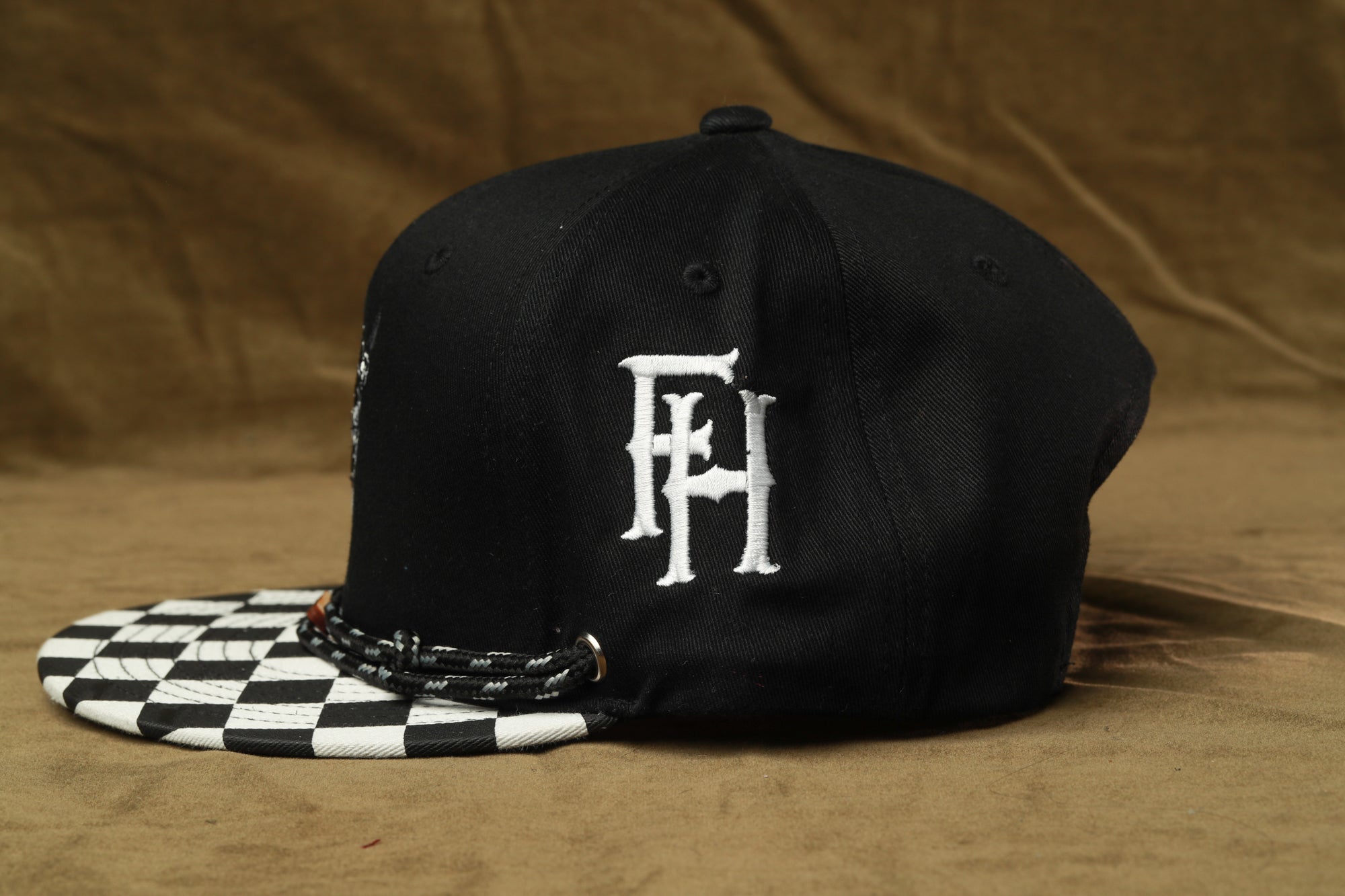 A black baseball cap with a white logo on the front, placed on a brown surface.