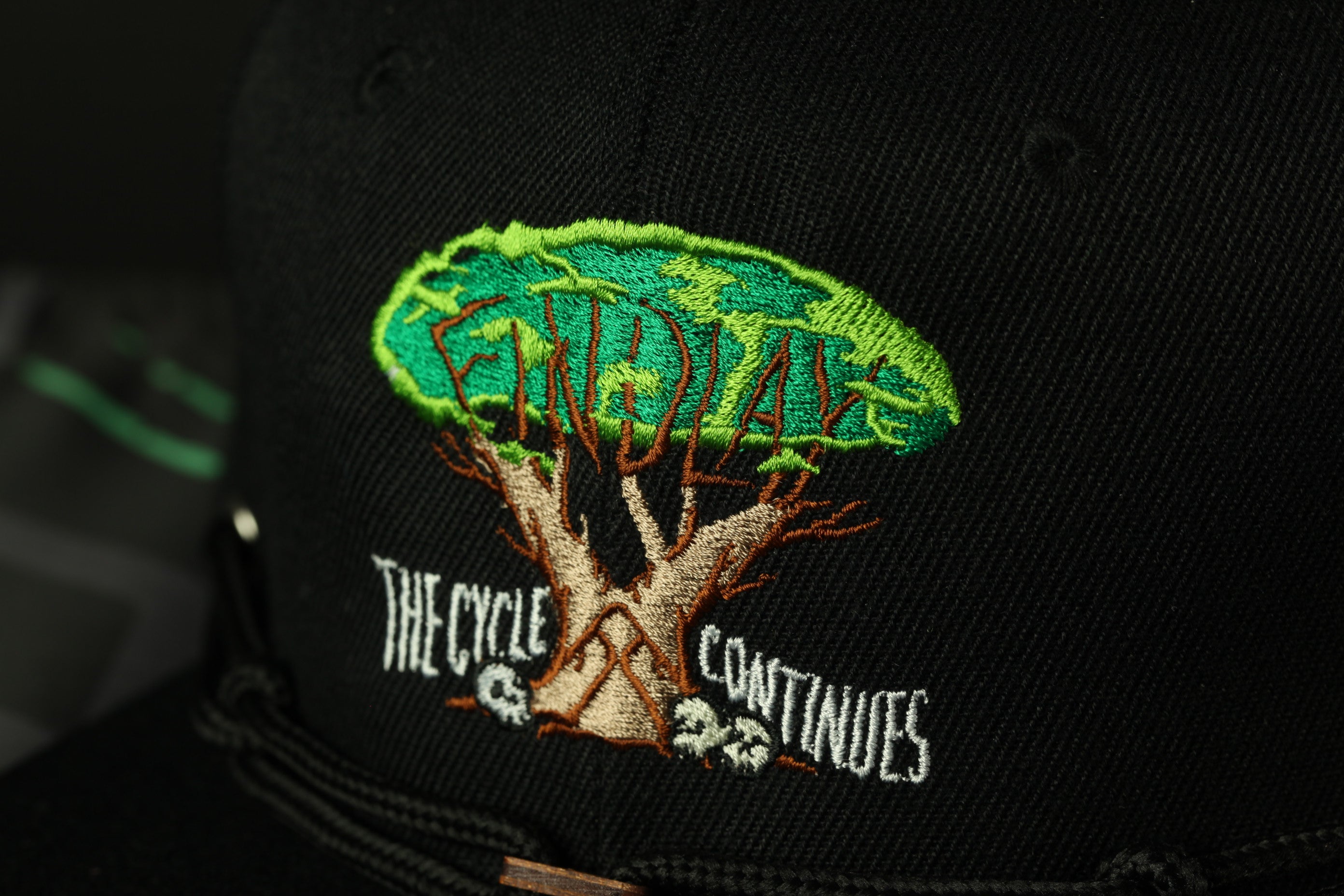 a close-up view of a black baseball cap with a green tree design and text embroidered on it.