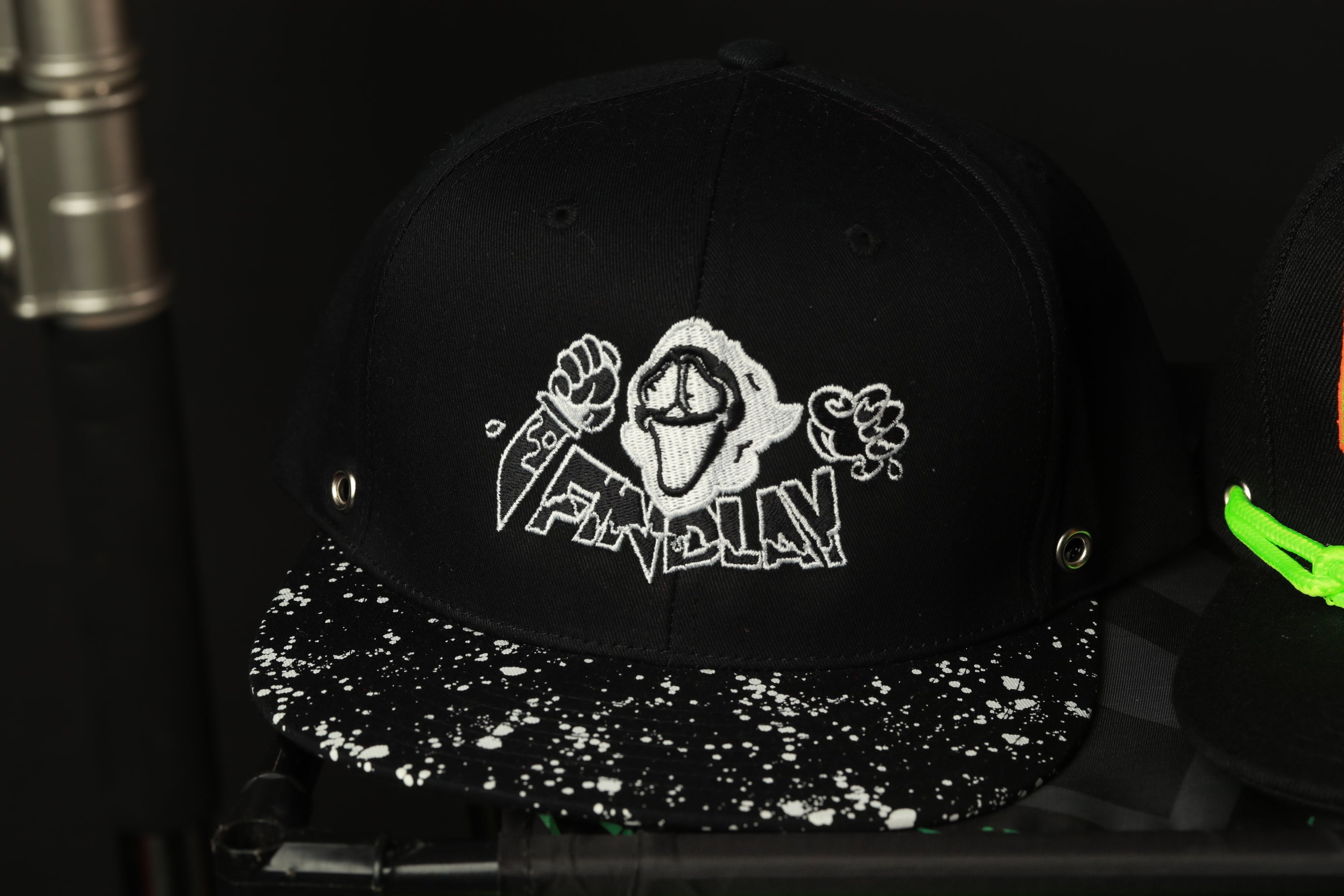 A black baseball cap with a white speckled pattern and a graphic design on the front.