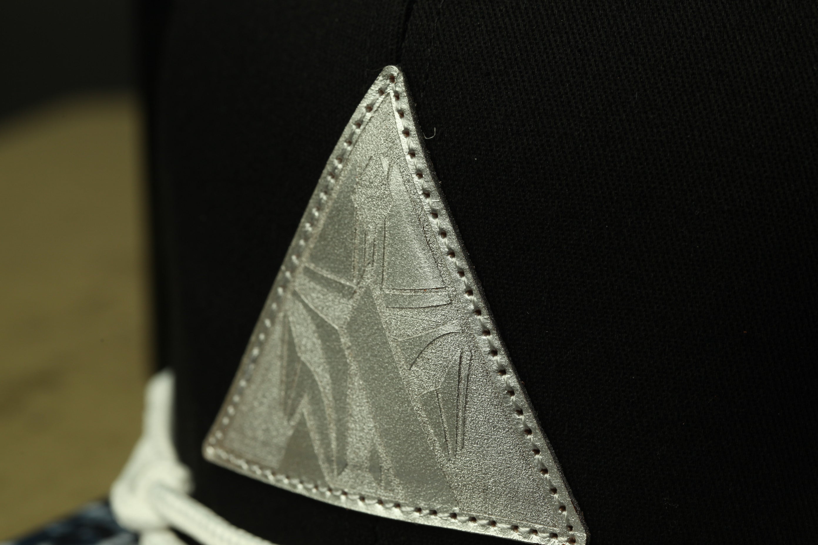 A close-up view of a black fabric with a silver triangular logo or emblem on it.