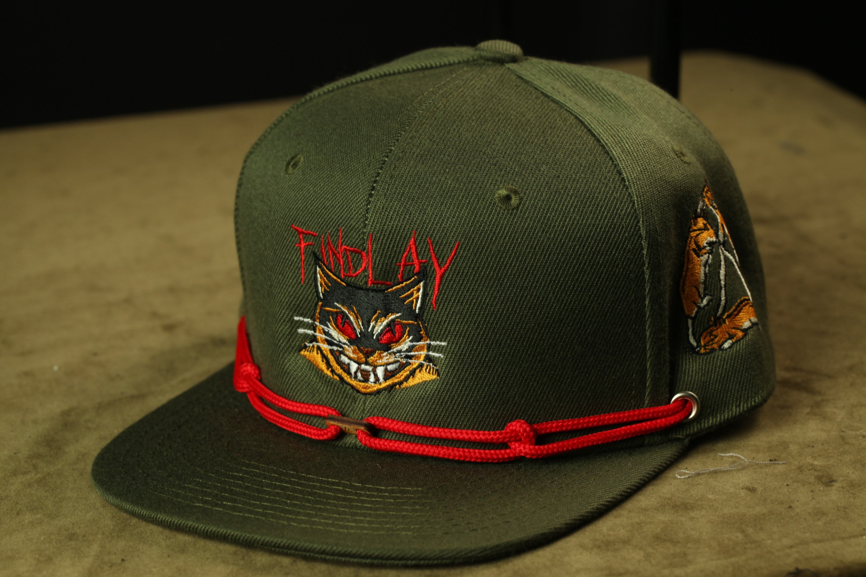 A green baseball cap with a cat design and the text "Findlay" printed on it.