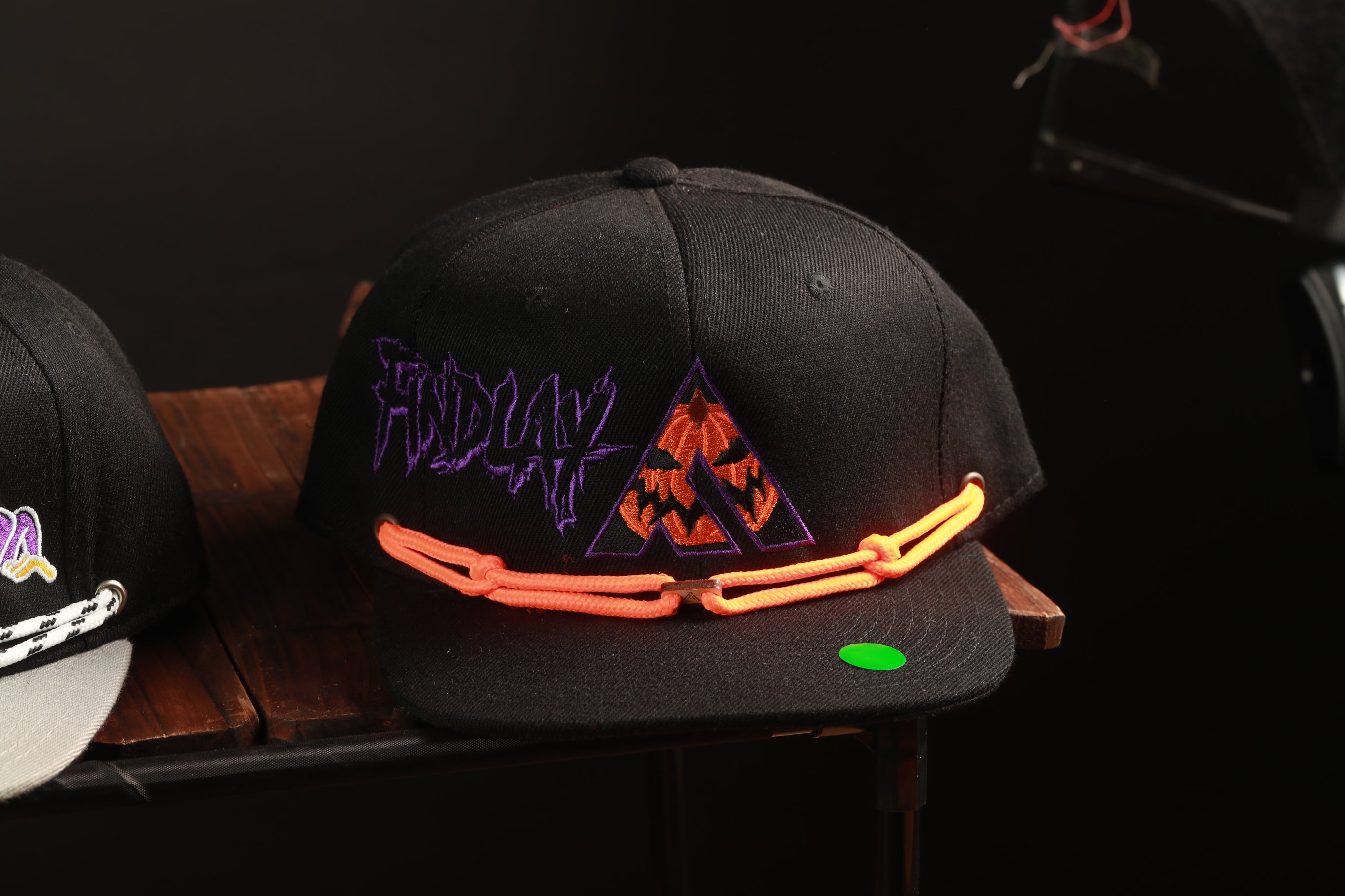 A black baseball cap with a pumpkin and chains design, sitting on a wooden surface.