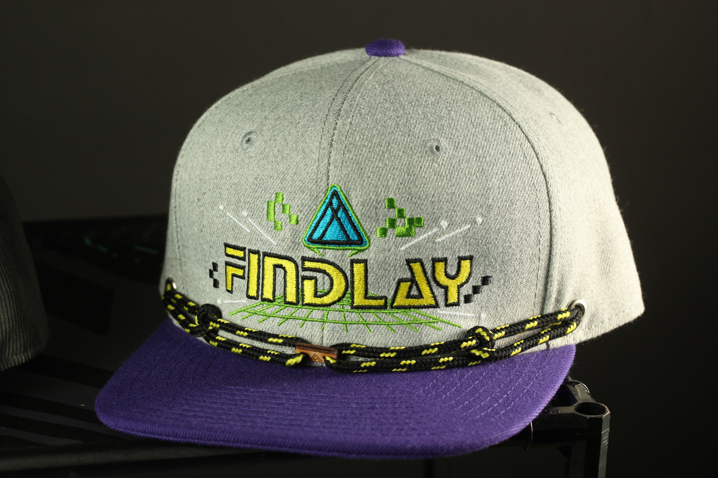 A gray baseball cap with a purple brim and a black and yellow lanyard.