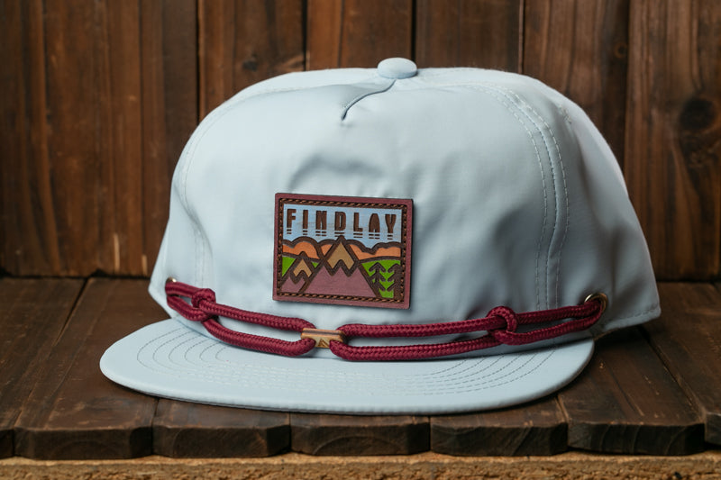 A light blue baseball cap with a red band and a patch on the front, sitting on a wooden surface.
