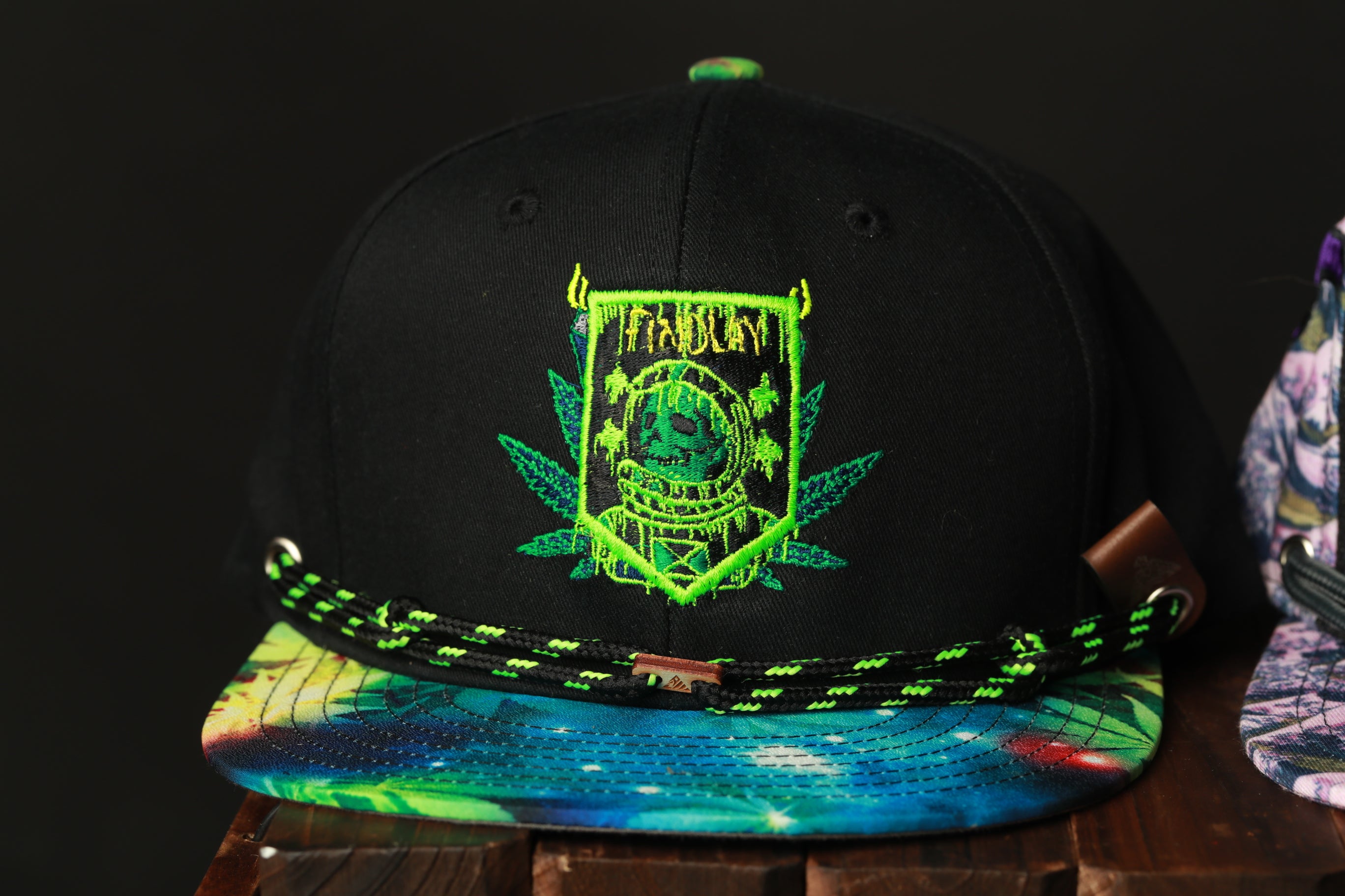 A black baseball cap with a colorful, tie-dye pattern and a green and black embroidered design on the front.
