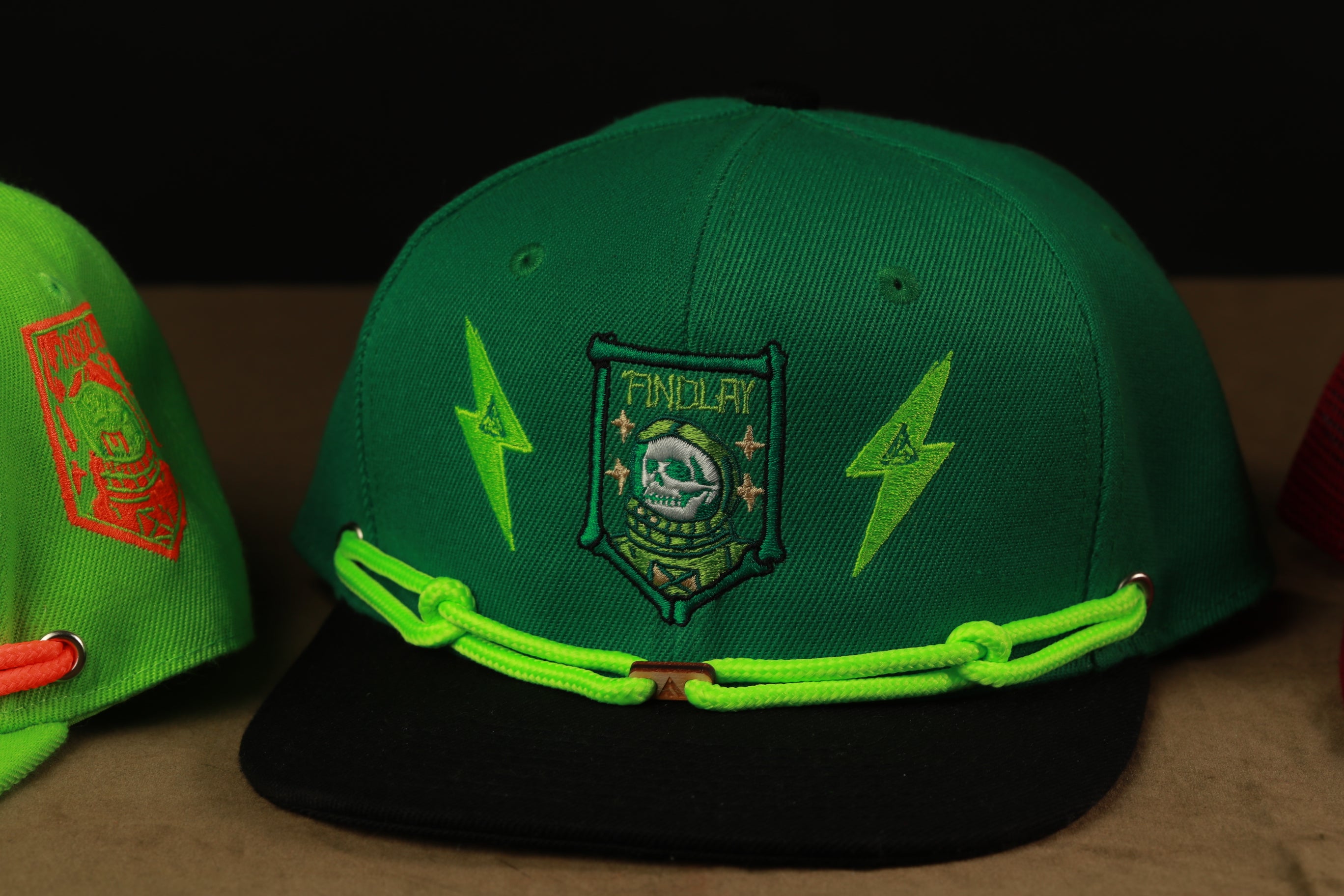 A green baseball cap with a black brim and a green and yellow emblem featuring a skull and lightning bolt design.
