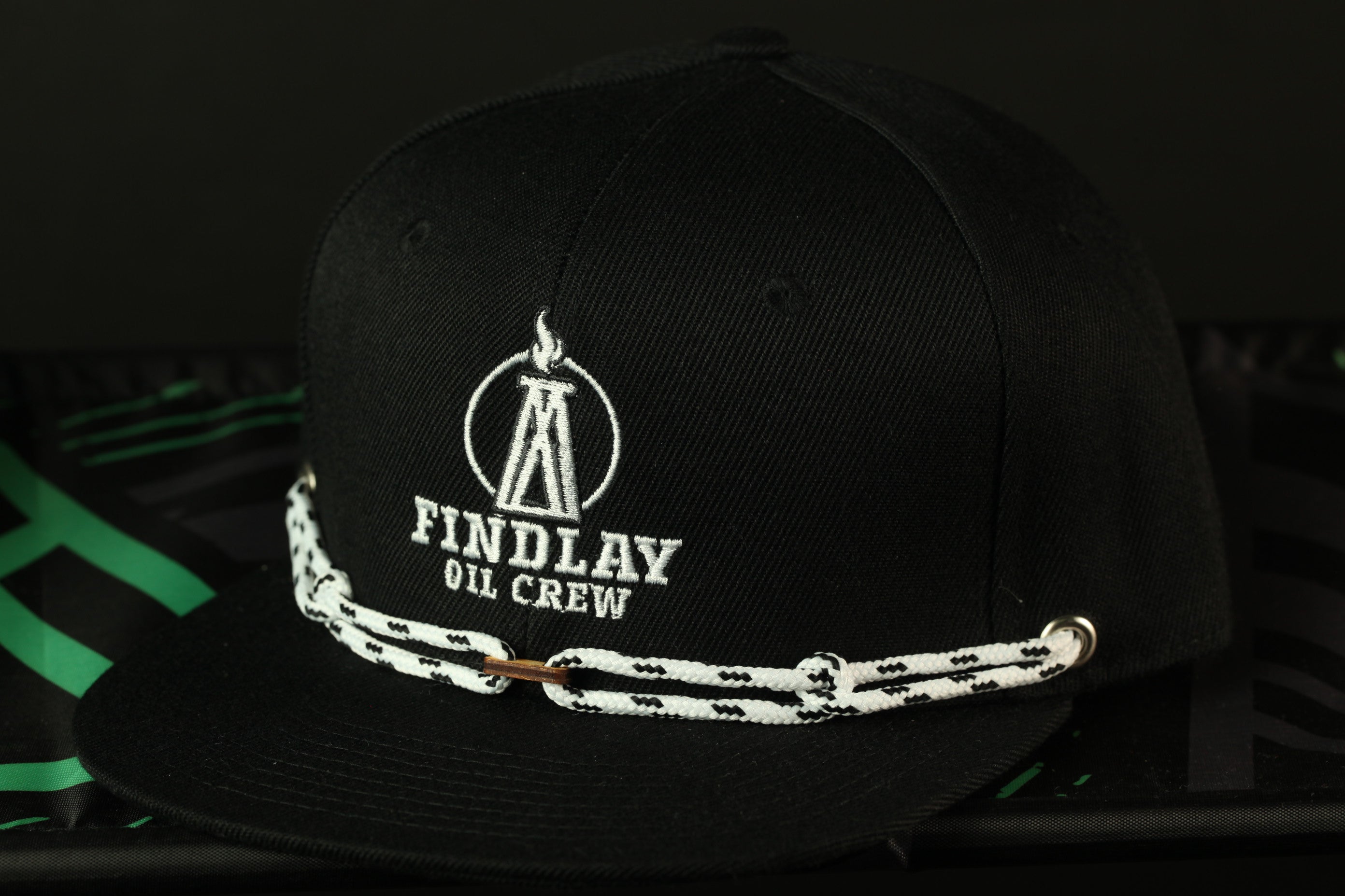 A black baseball cap with white text and logos, including the text "FINDLAY OIL CREW" and a flame symbol.