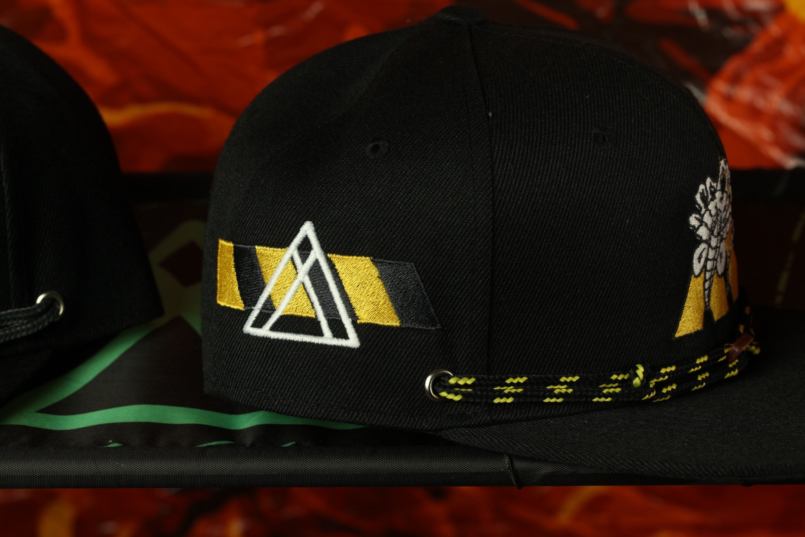 A black baseball cap with a yellow and black geometric pattern on the front, featuring a triangular design and a flower-like pattern on the side.