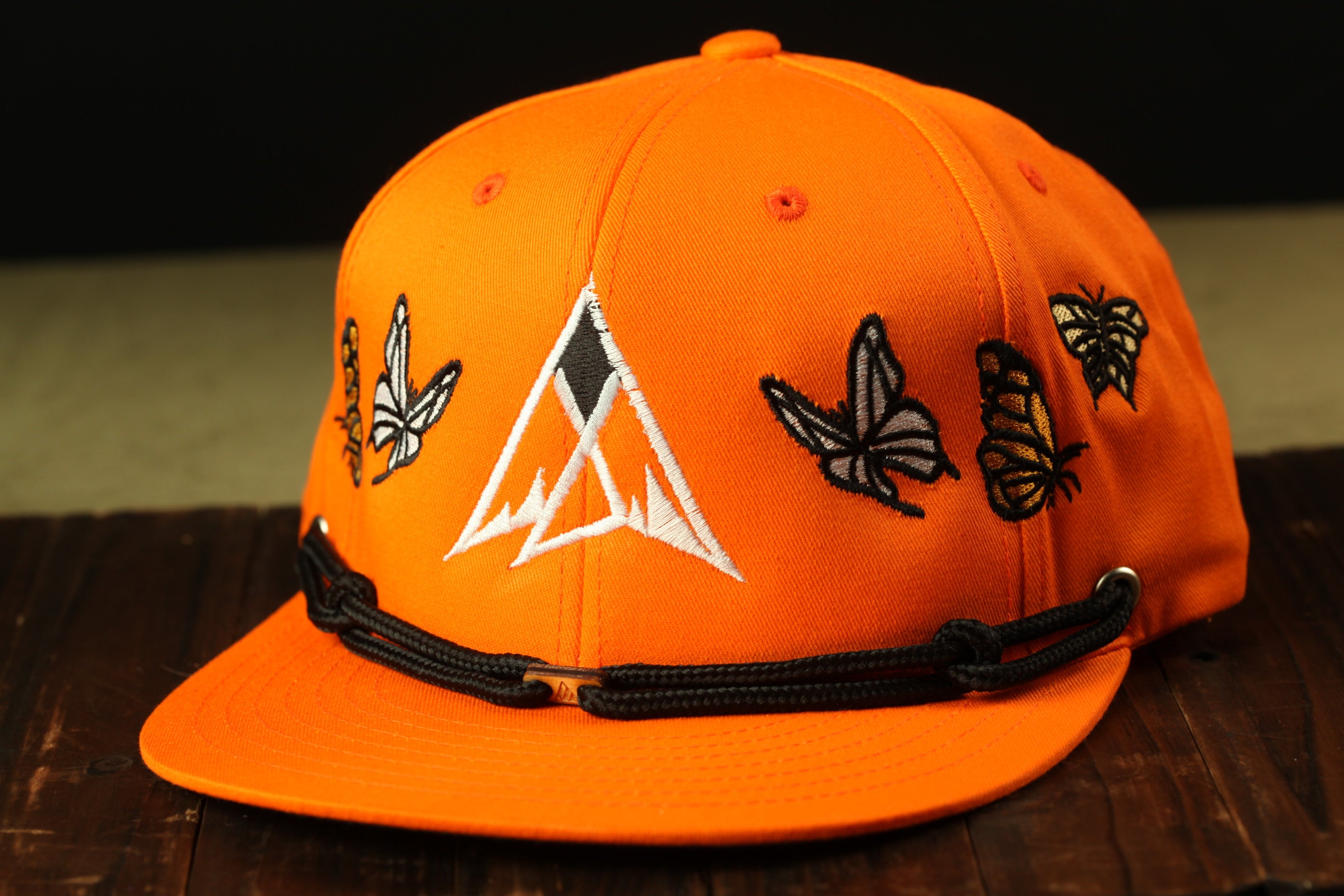 An orange baseball cap with a black strap and white and black butterfly designs on the front.