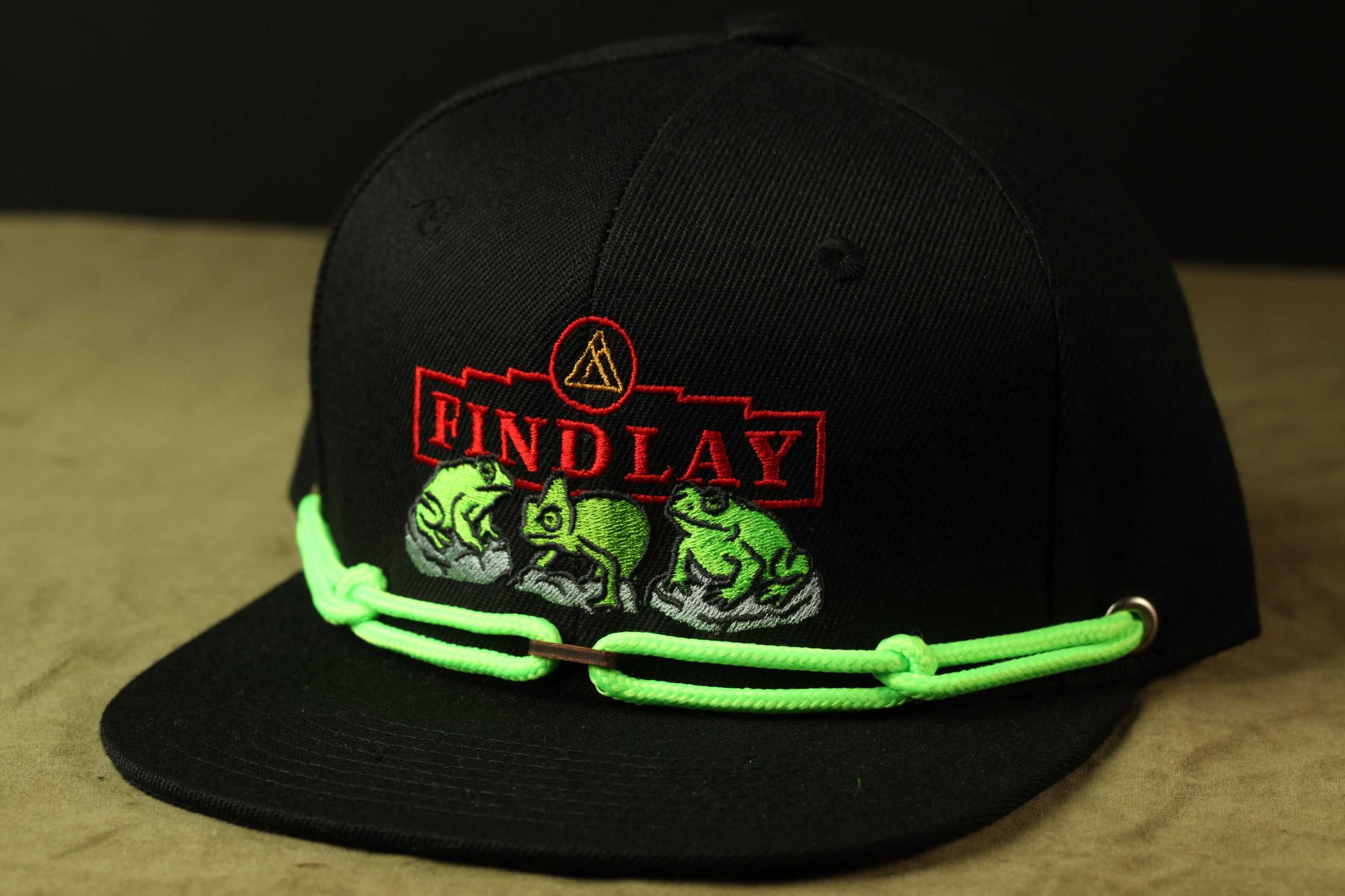 A black baseball cap with a green string and a logo on it.