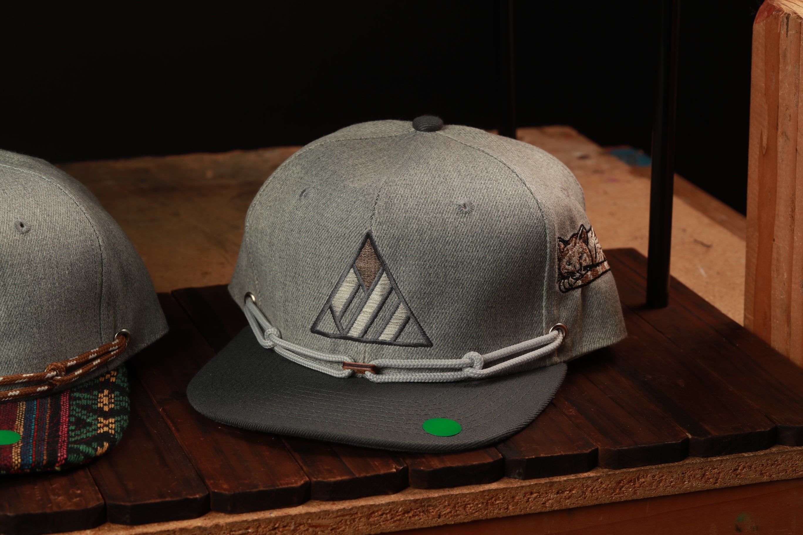 A gray baseball cap with a triangular logo on the front, displayed on a wooden surface.