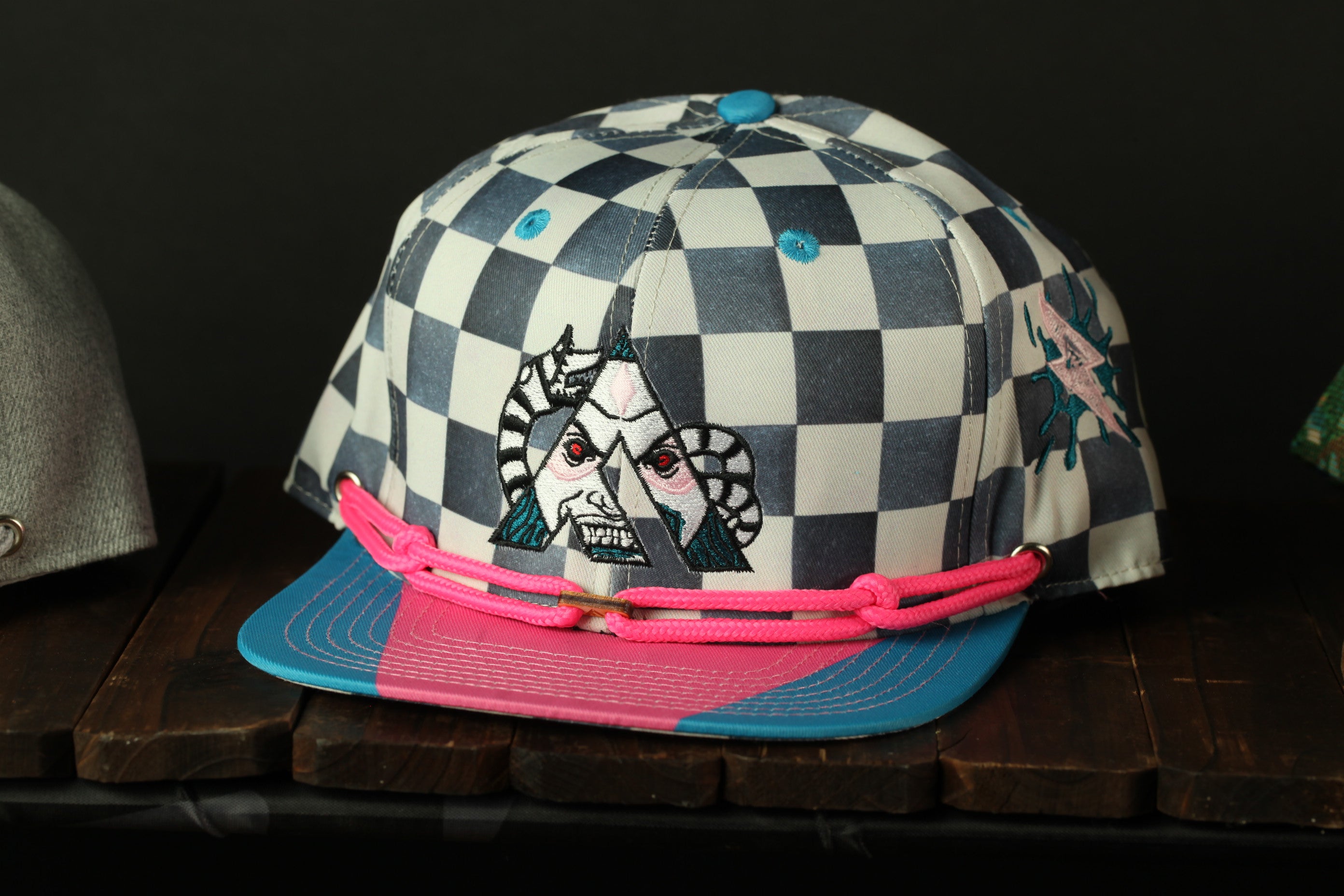 A colorful baseball cap with a checkered pattern and a graphic design on the front, sitting on a wooden surface.