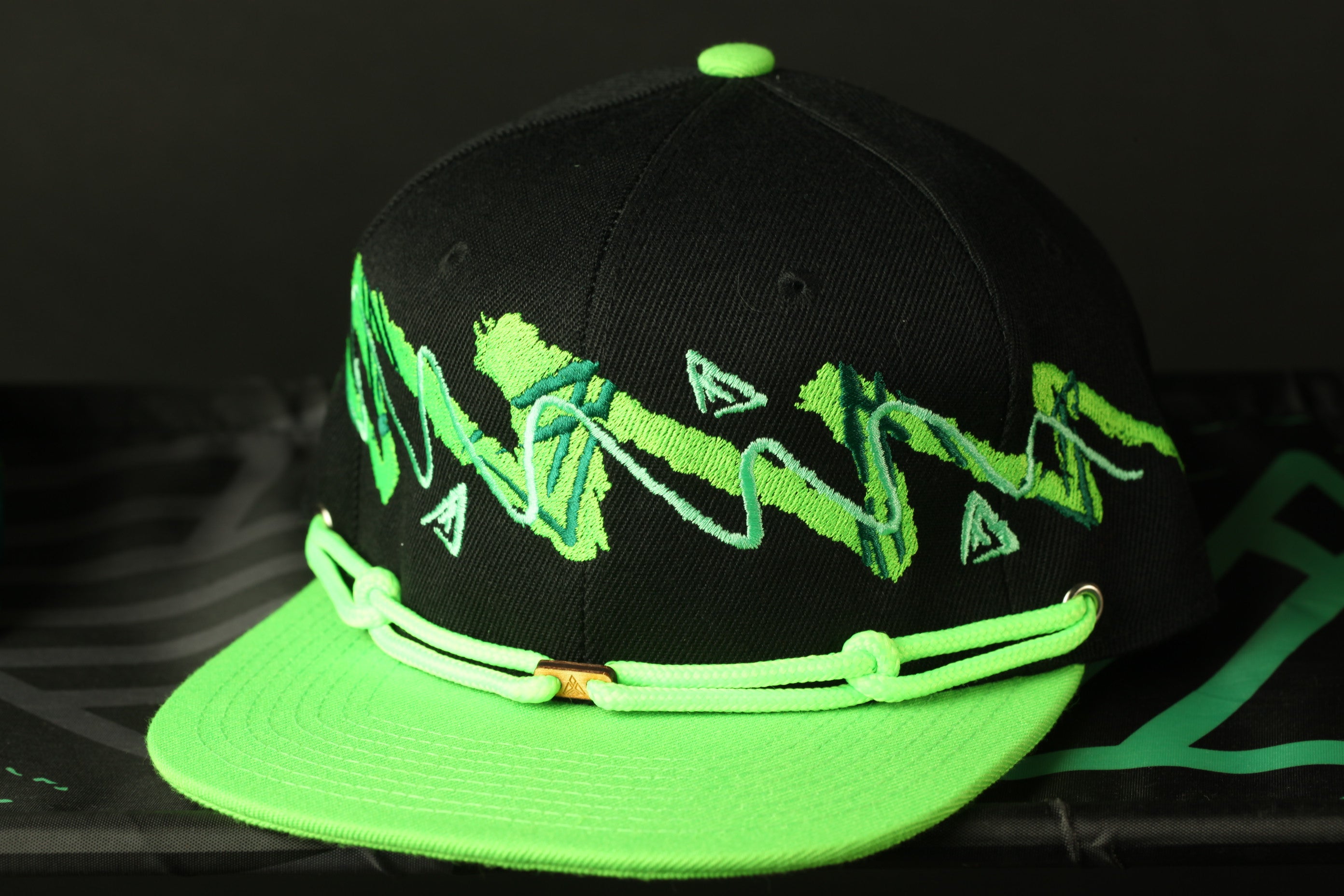 A black baseball cap with green and white designs on it, placed on a black surface.