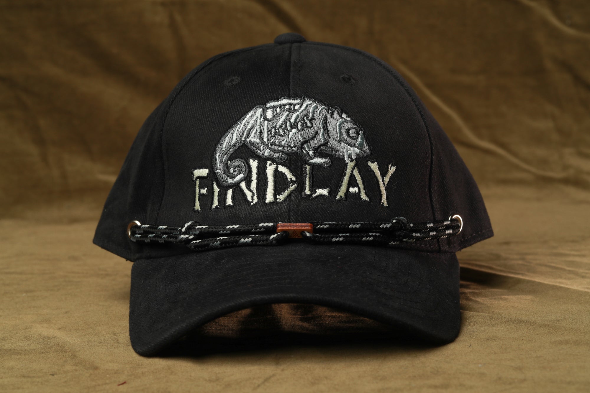 A black baseball cap with a white embroidered design of a chameleon and the word "FRIDAY" printed on it.