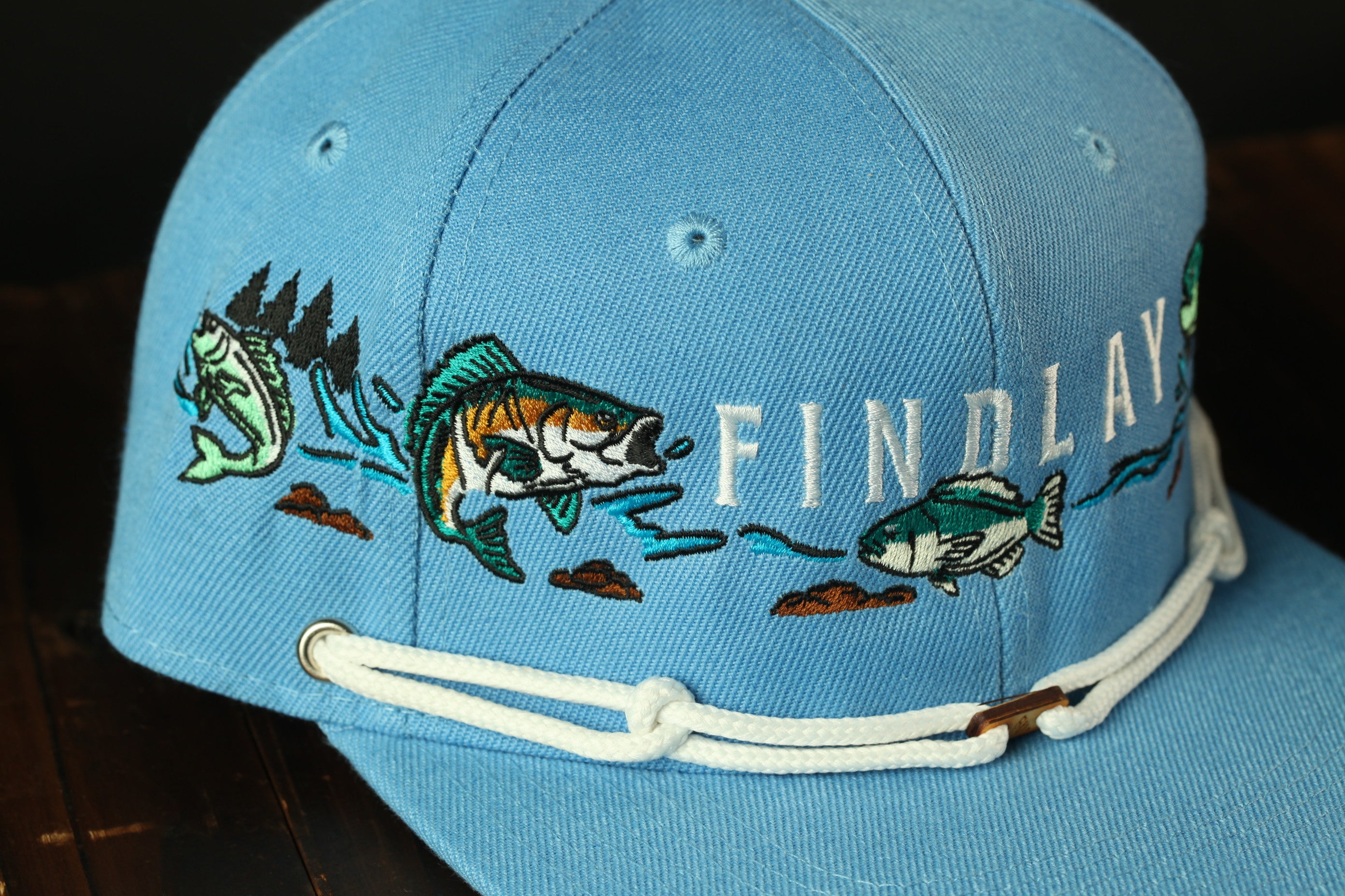 A blue baseball cap with embroidered fish designs and the word "FINDlay" printed on it.