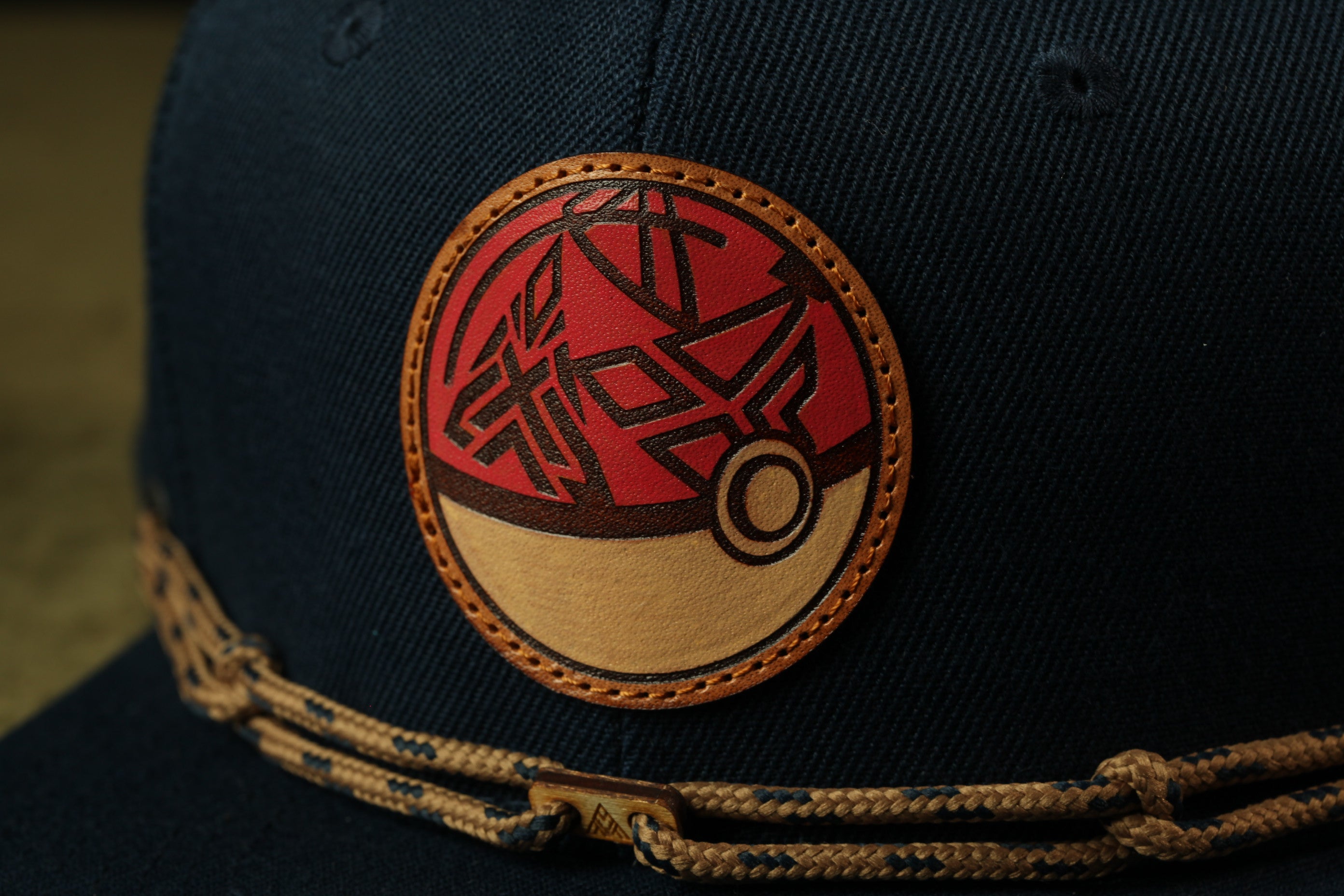 A close-up view of a dark blue baseball cap with a circular patch featuring a red and black design.