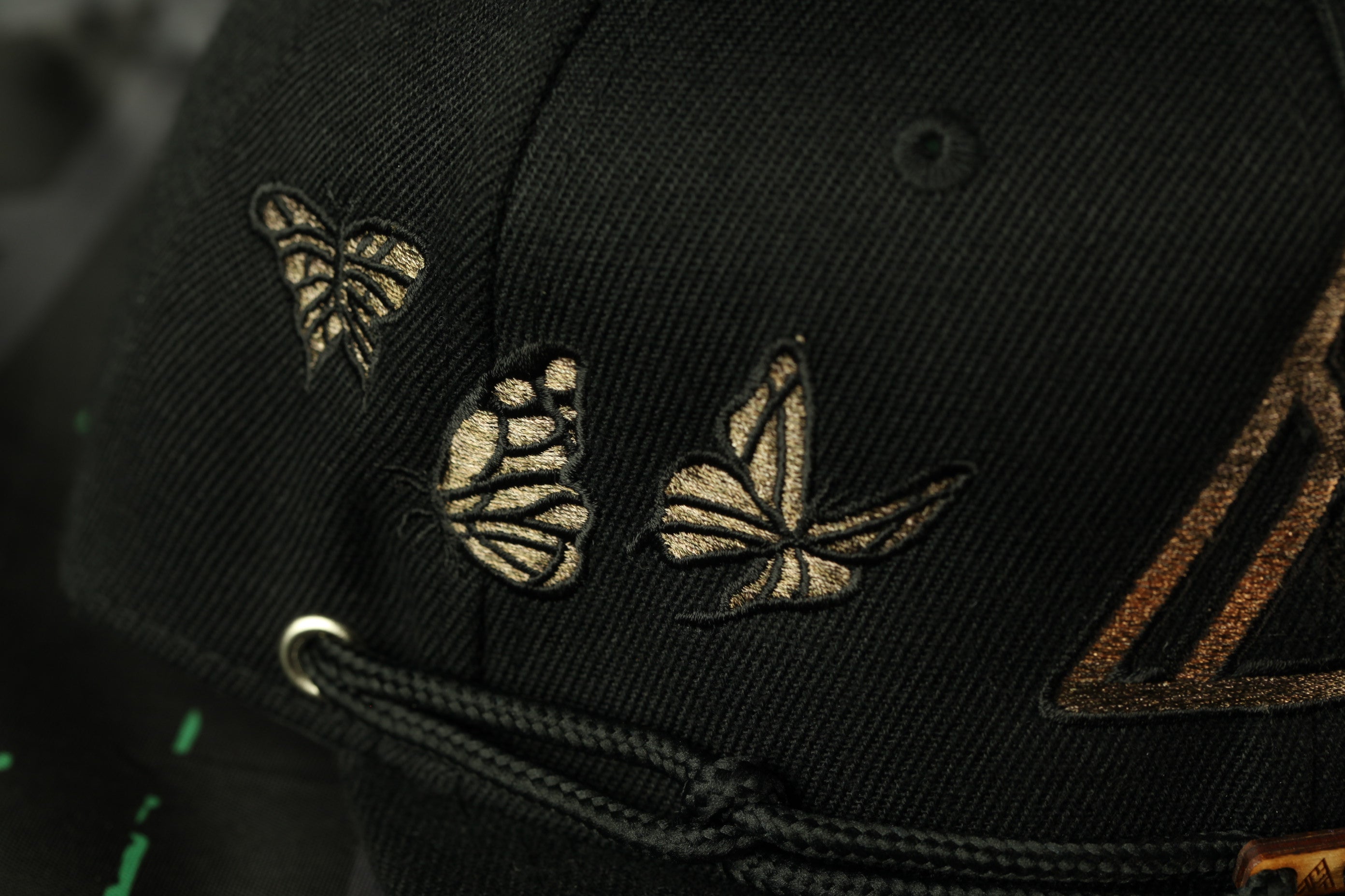 A close-up view of a black baseball cap with gold embroidered butterflies on the front.