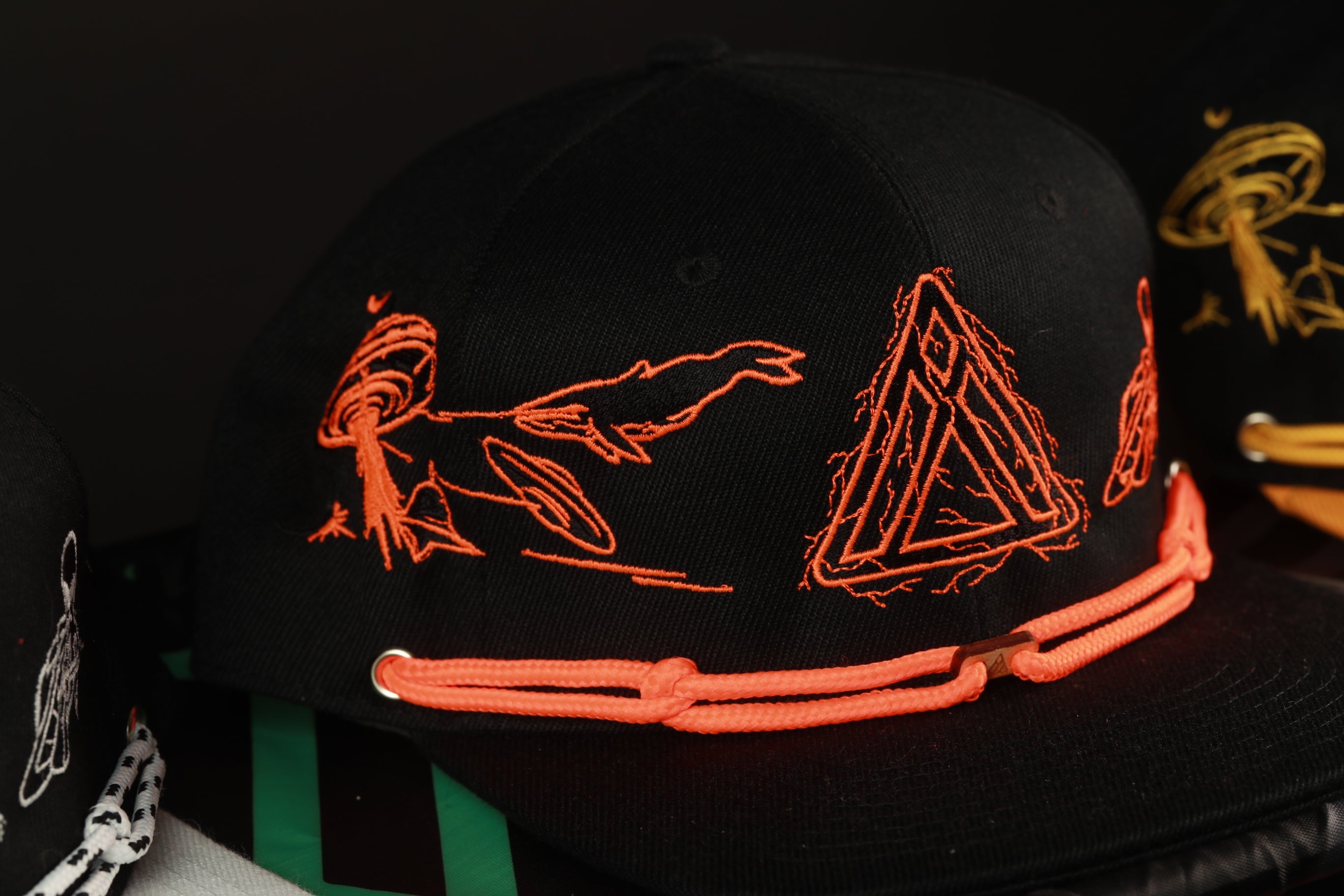 A close-up view of a black baseball cap with orange and black embroidered designs, including a triangle and a bird.