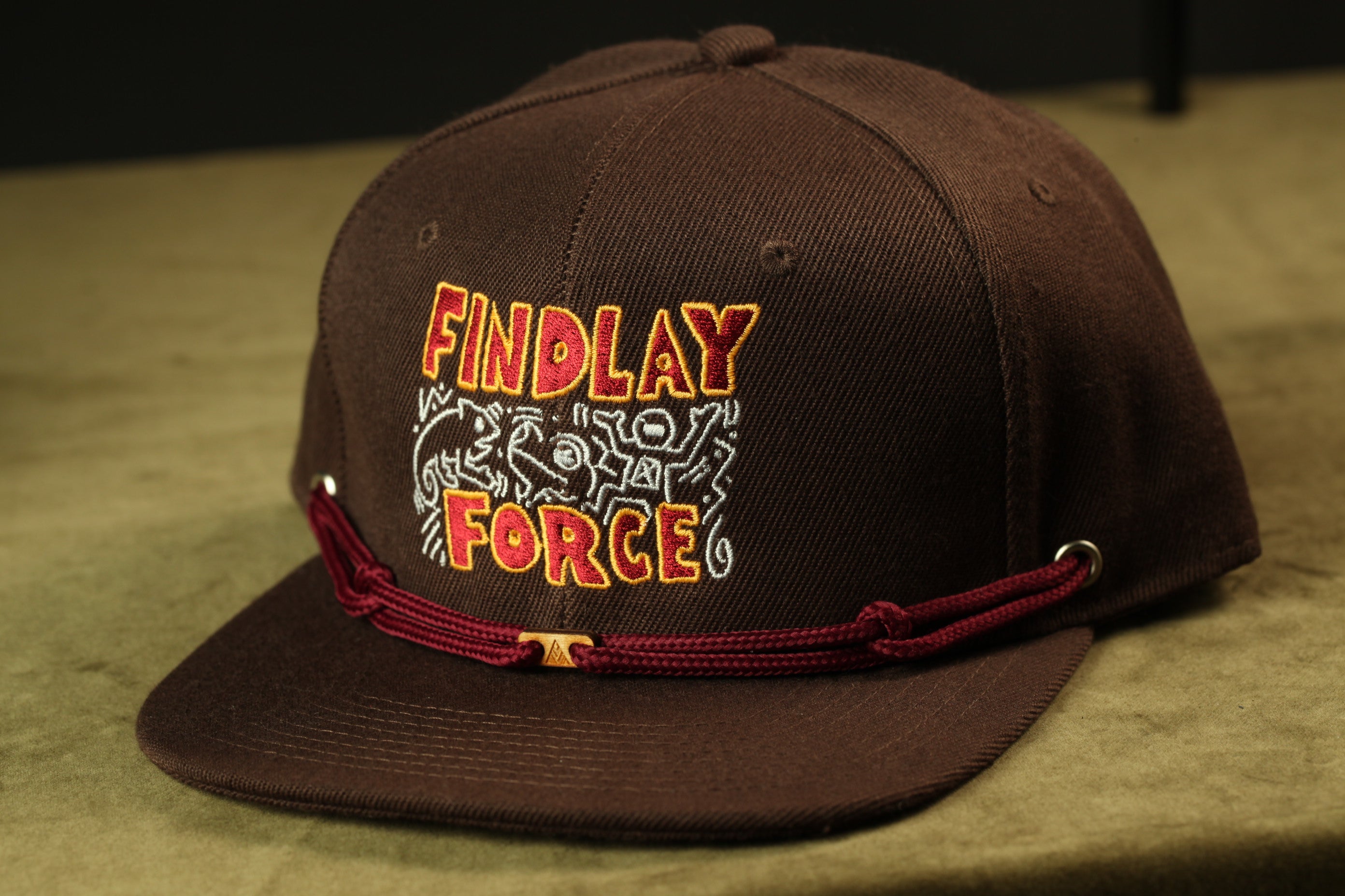 A brown baseball cap with the text "FINDLAY FORCE" printed on it.