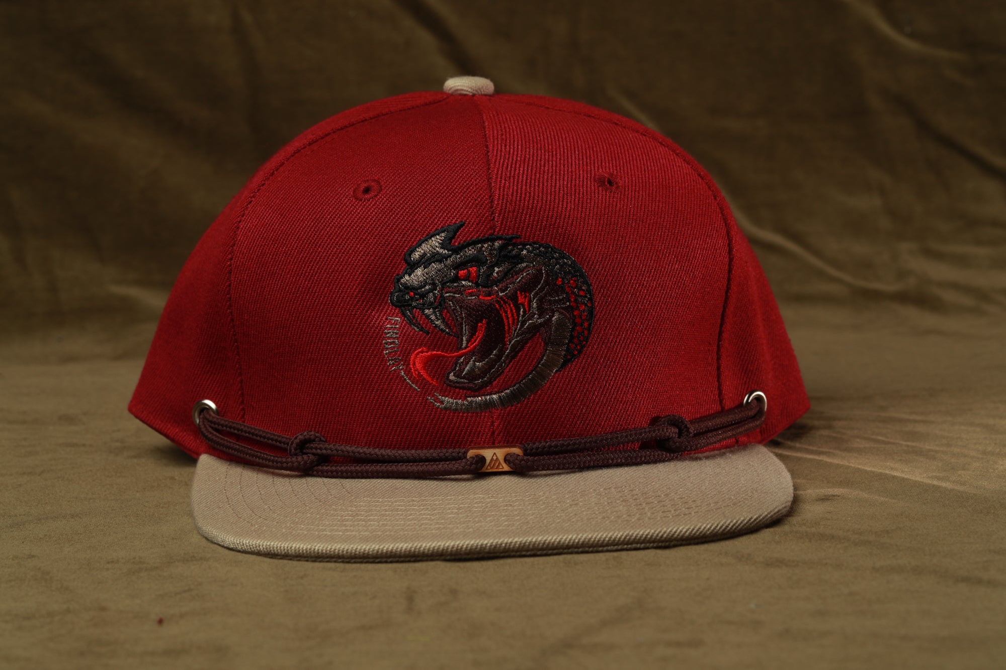 A red baseball cap with a black and red logo on the front, featuring a stylized snake or alligator design.