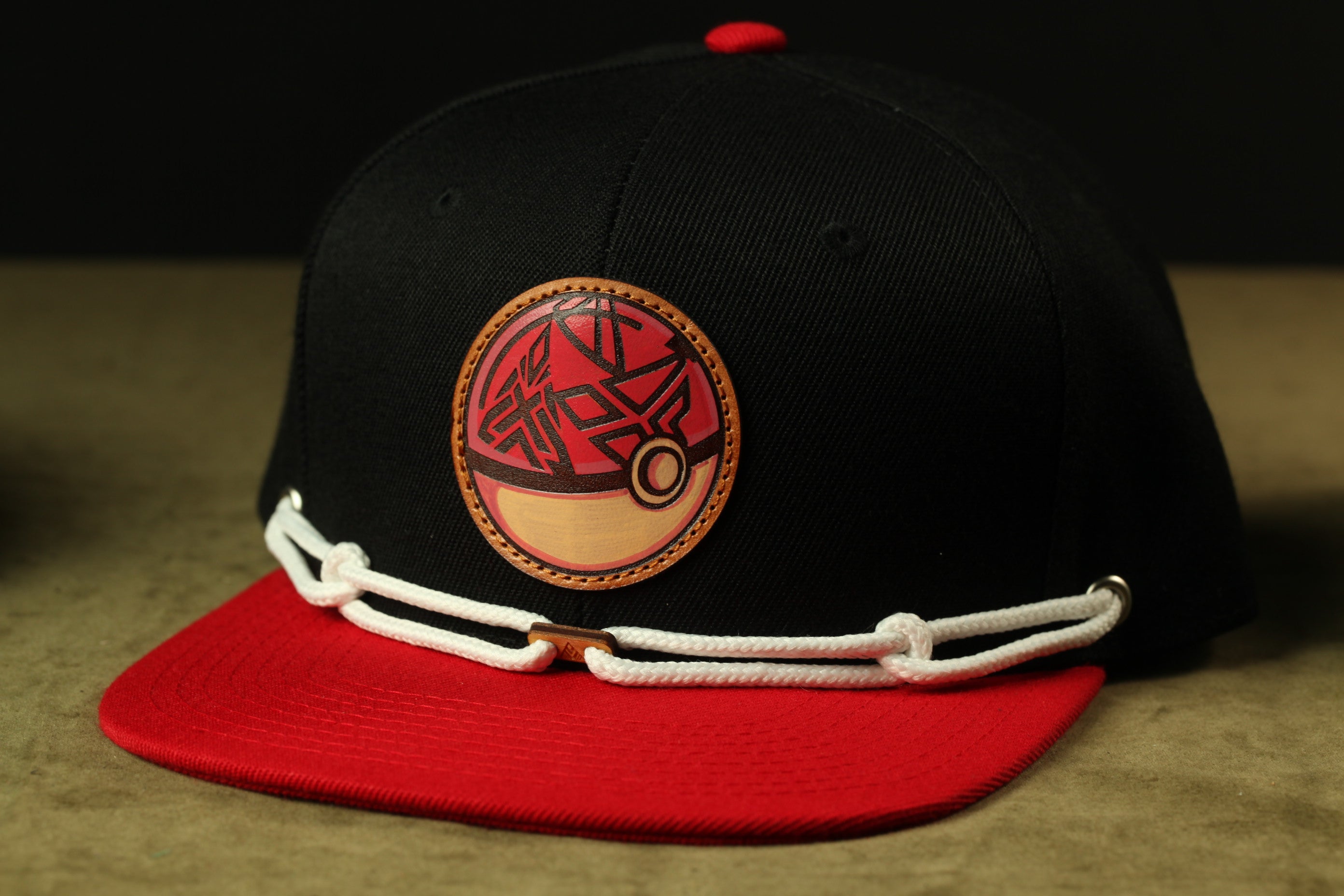 A black baseball cap with a red and white design on the front, featuring a circular emblem with a red and gold pattern.