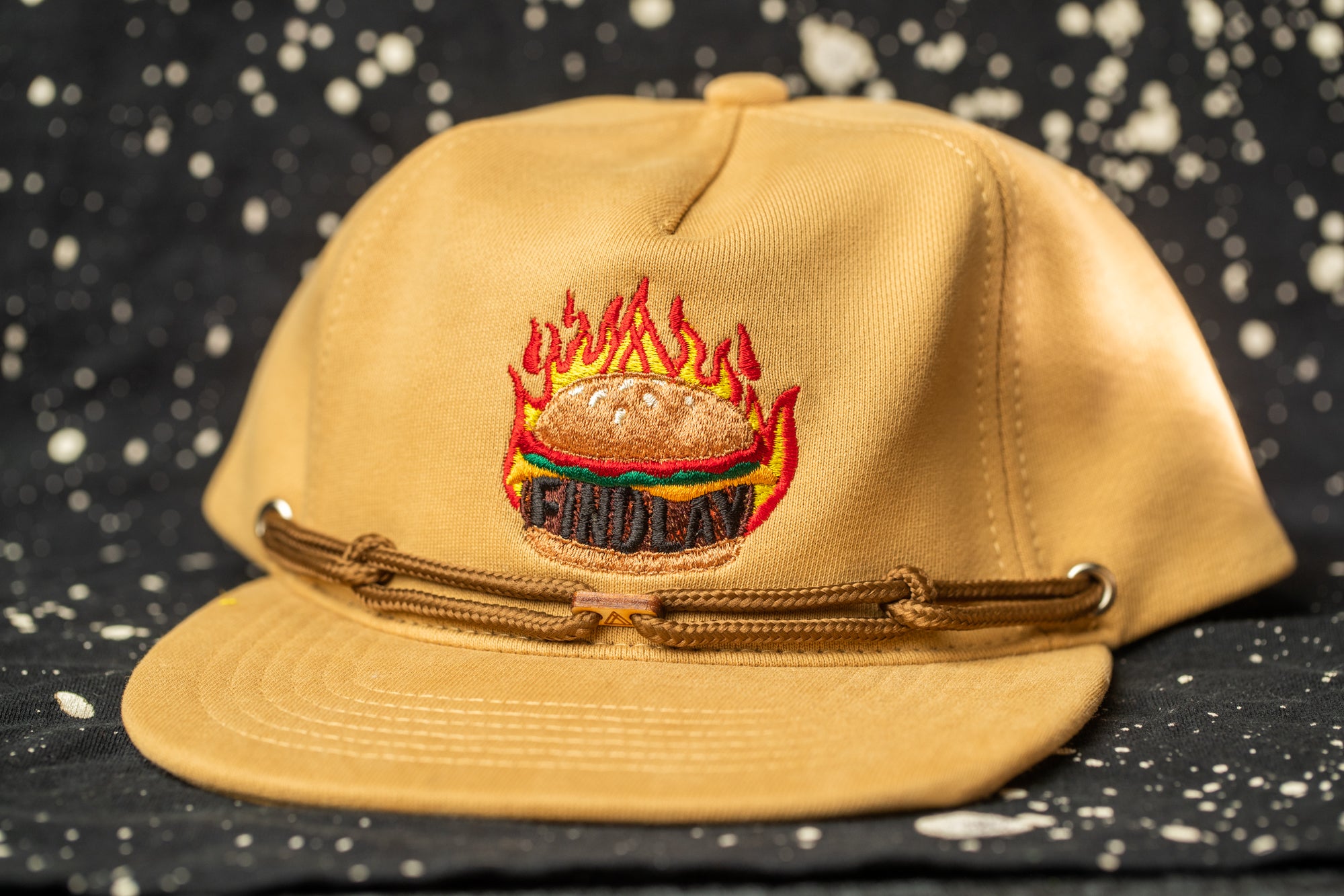 A tan baseball cap with a flame design on the front, featuring a hamburger and flames.